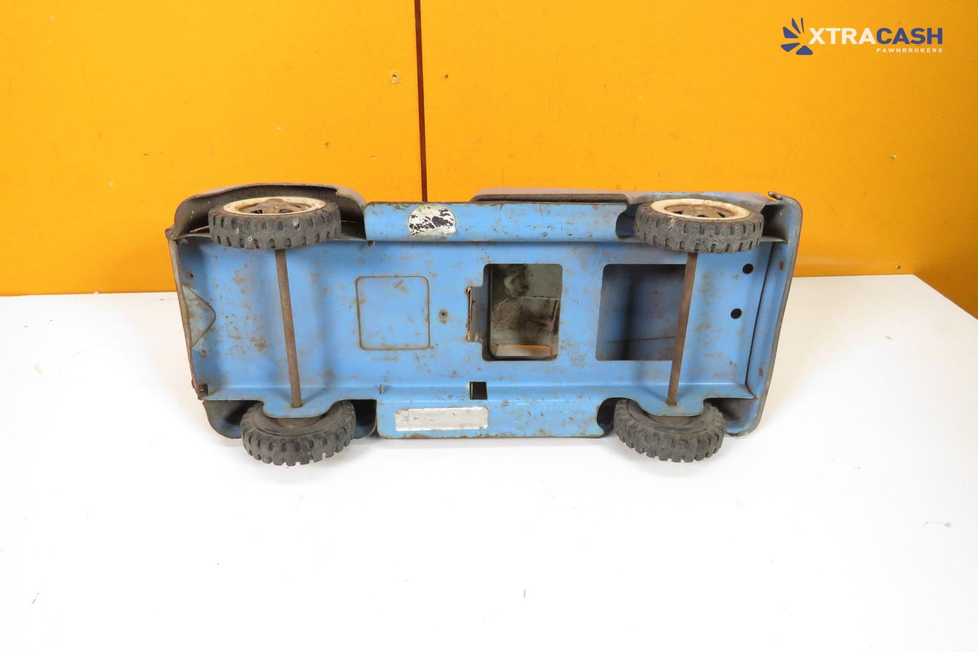 Blue weathered toy pickup truck on a white surface against an orange background