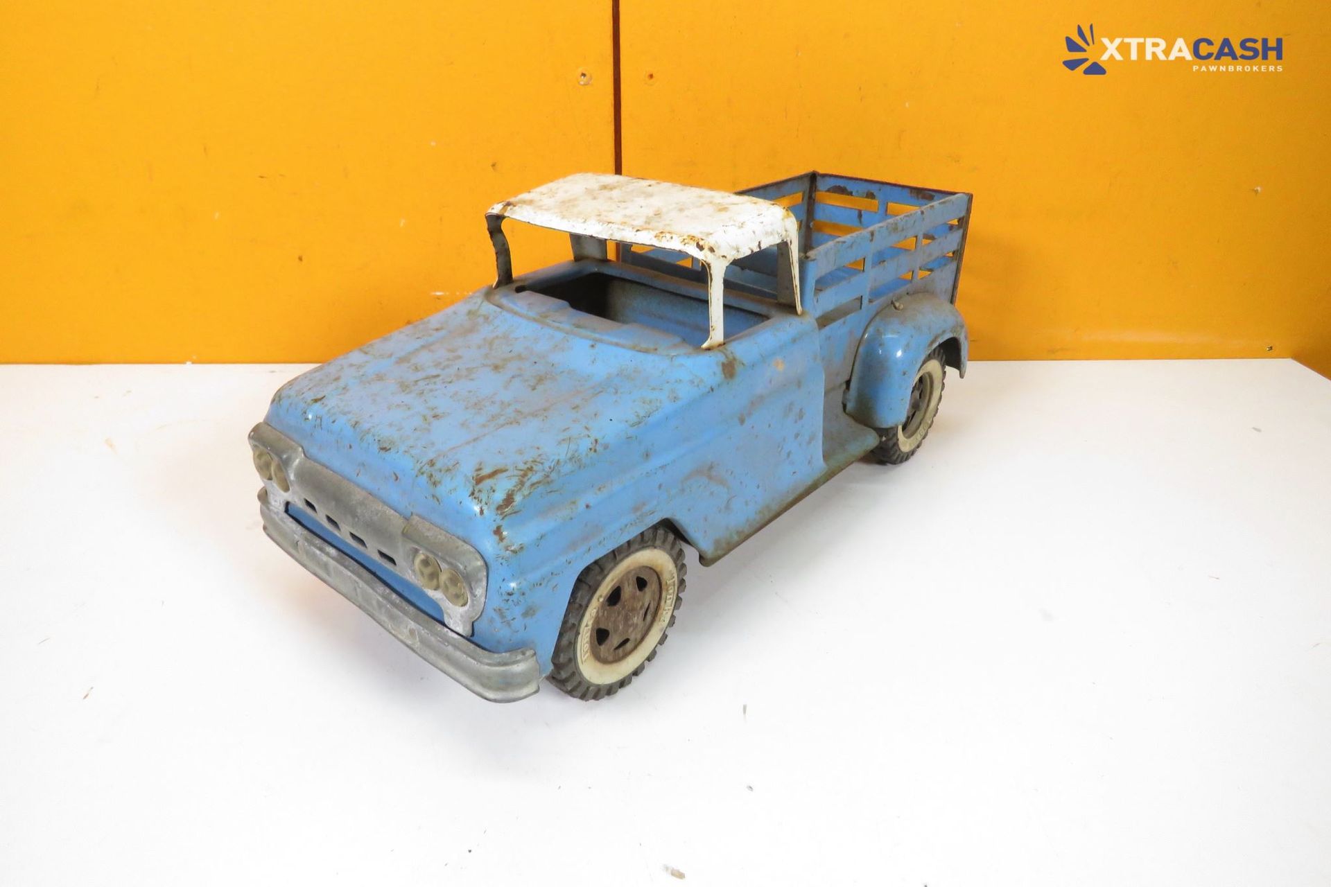 Blue weathered toy pickup truck on a white surface against an orange background