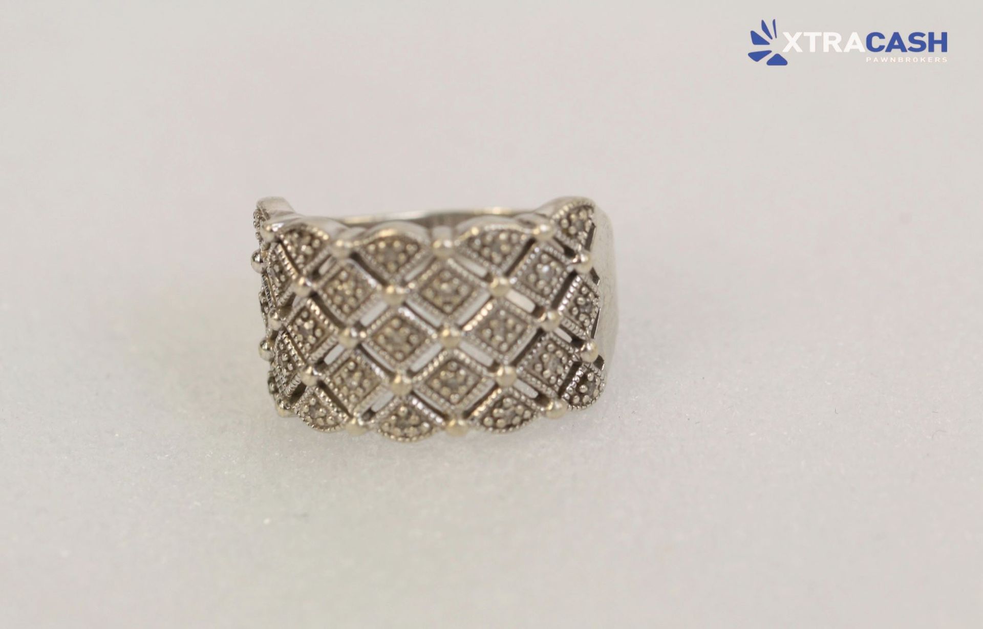 Silver diamond-pattern ring with sparkling stones on a plain light background