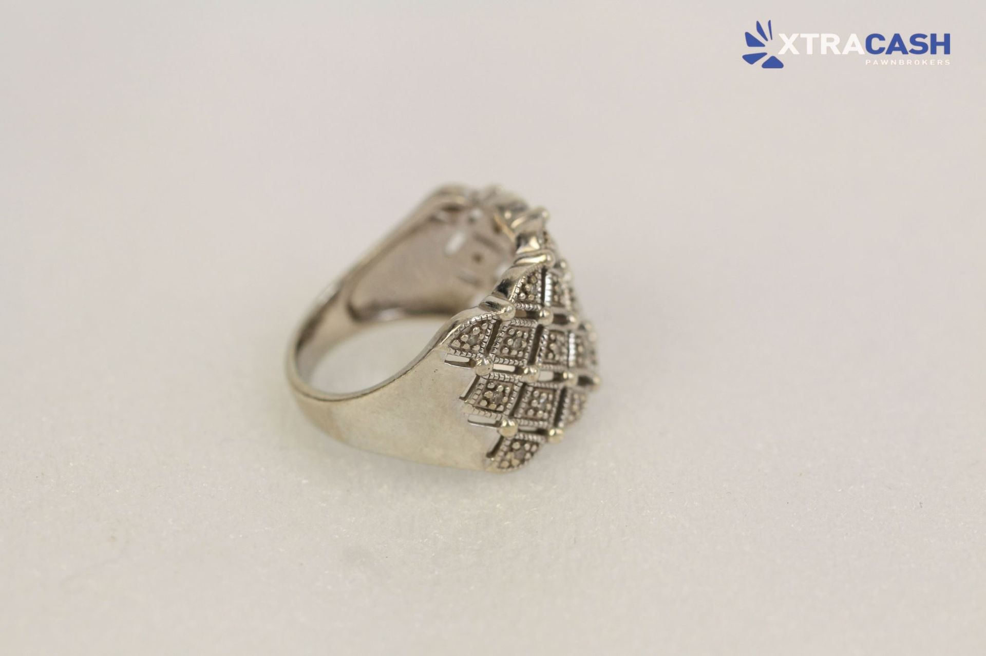 Silver diamond-pattern ring with sparkling stones on a plain light background