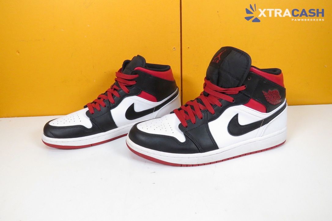 Pair of black, white, and red sneakers on a white surface against a yellow background.