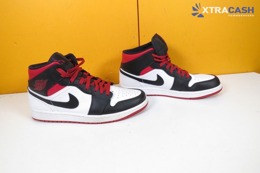 Pair of black, white, and red sneakers on a white surface against a yellow background.