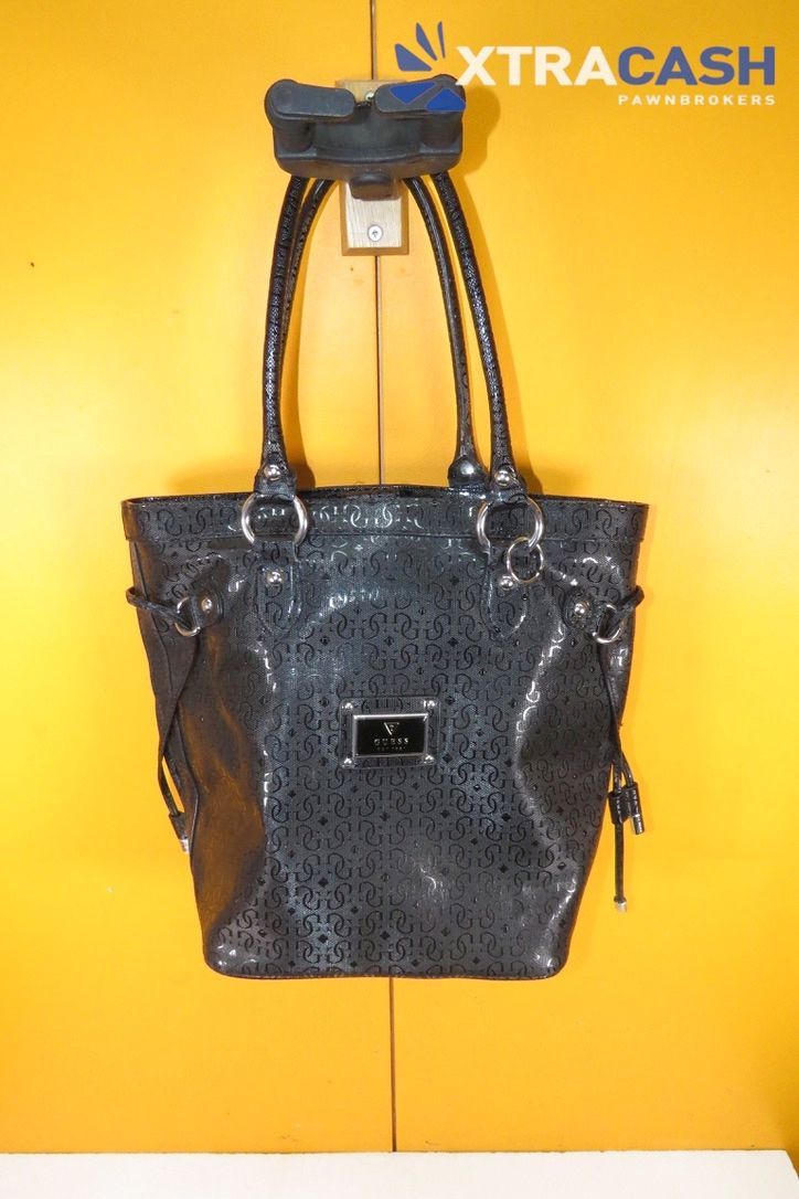 Black studded handbag with long straps hanging against a bright yellow wall.