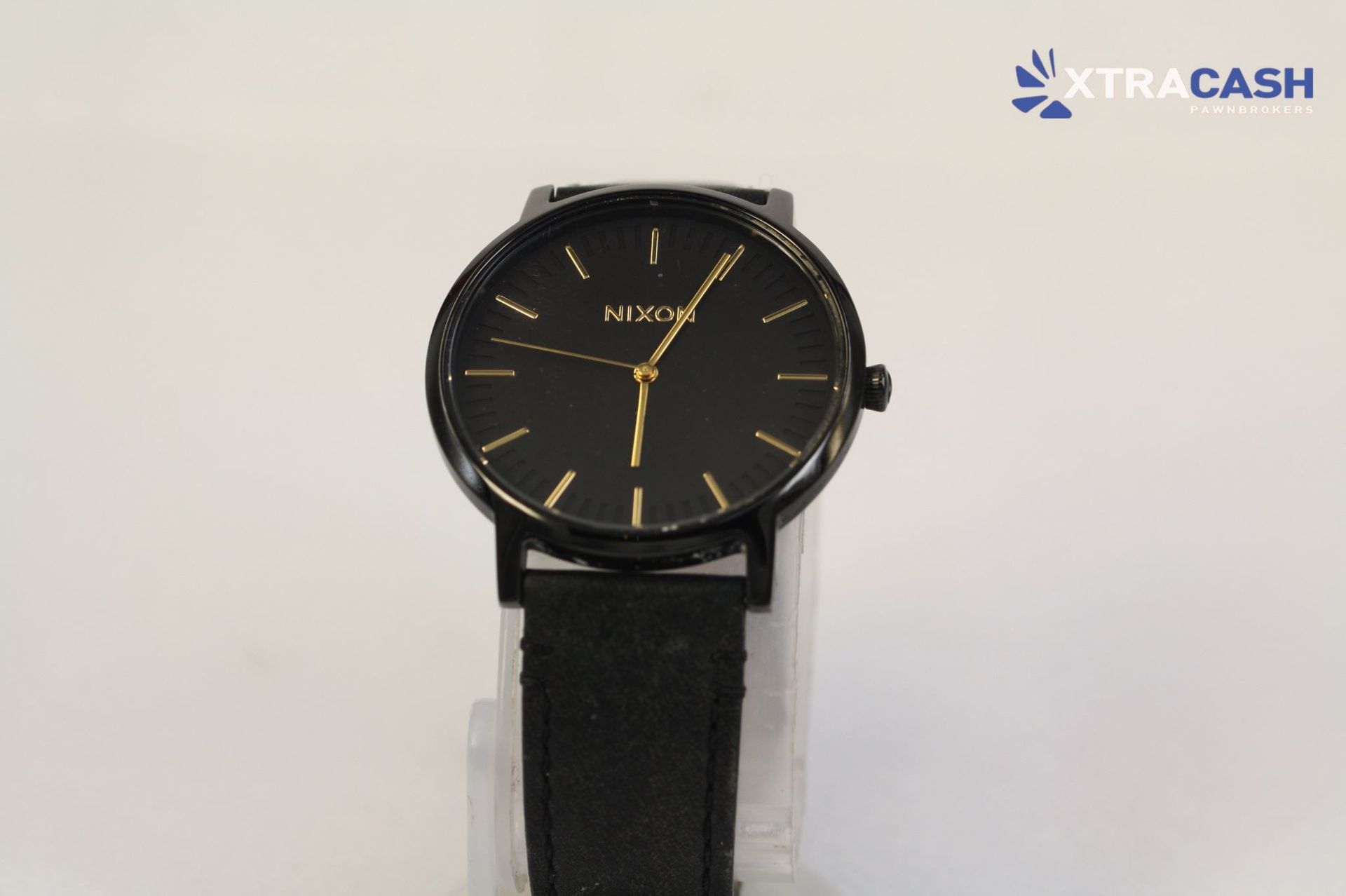 Black wristwatch with gold accents on a strap against a light background