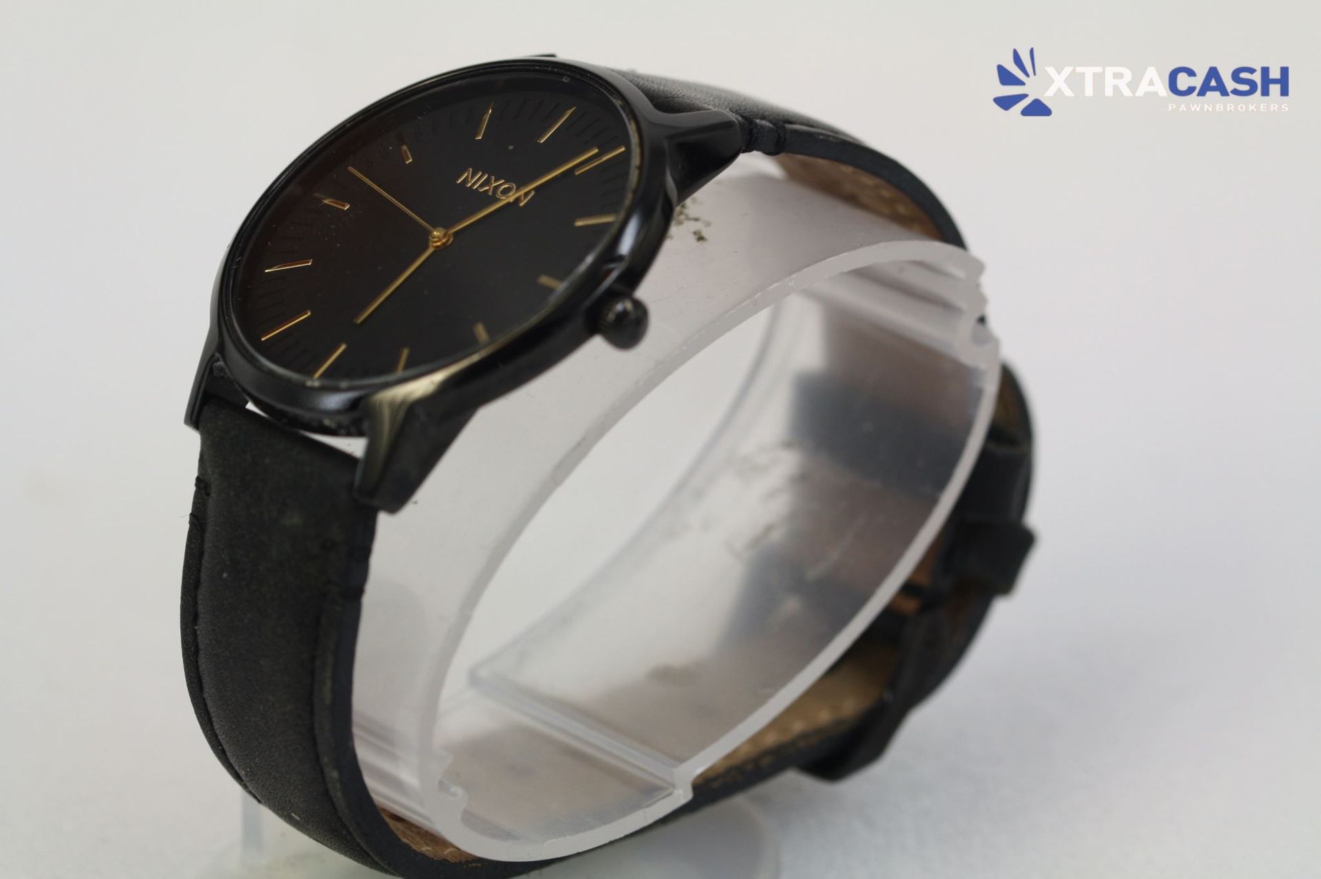 Black wristwatch with gold accents on a strap against a light background