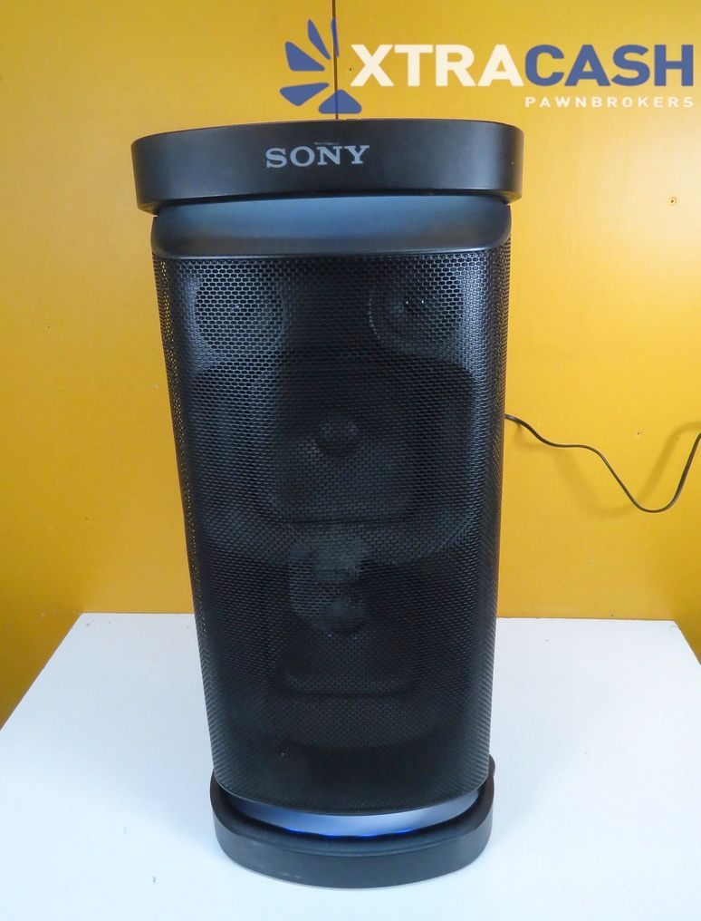 Black Sony portable speaker with blue base on a white table against a yellow wall.