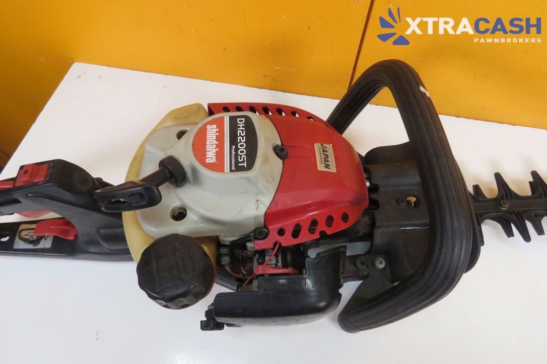 Gas-powered hedge trimmer on a white table against an orange wall with XTRACASH logo.