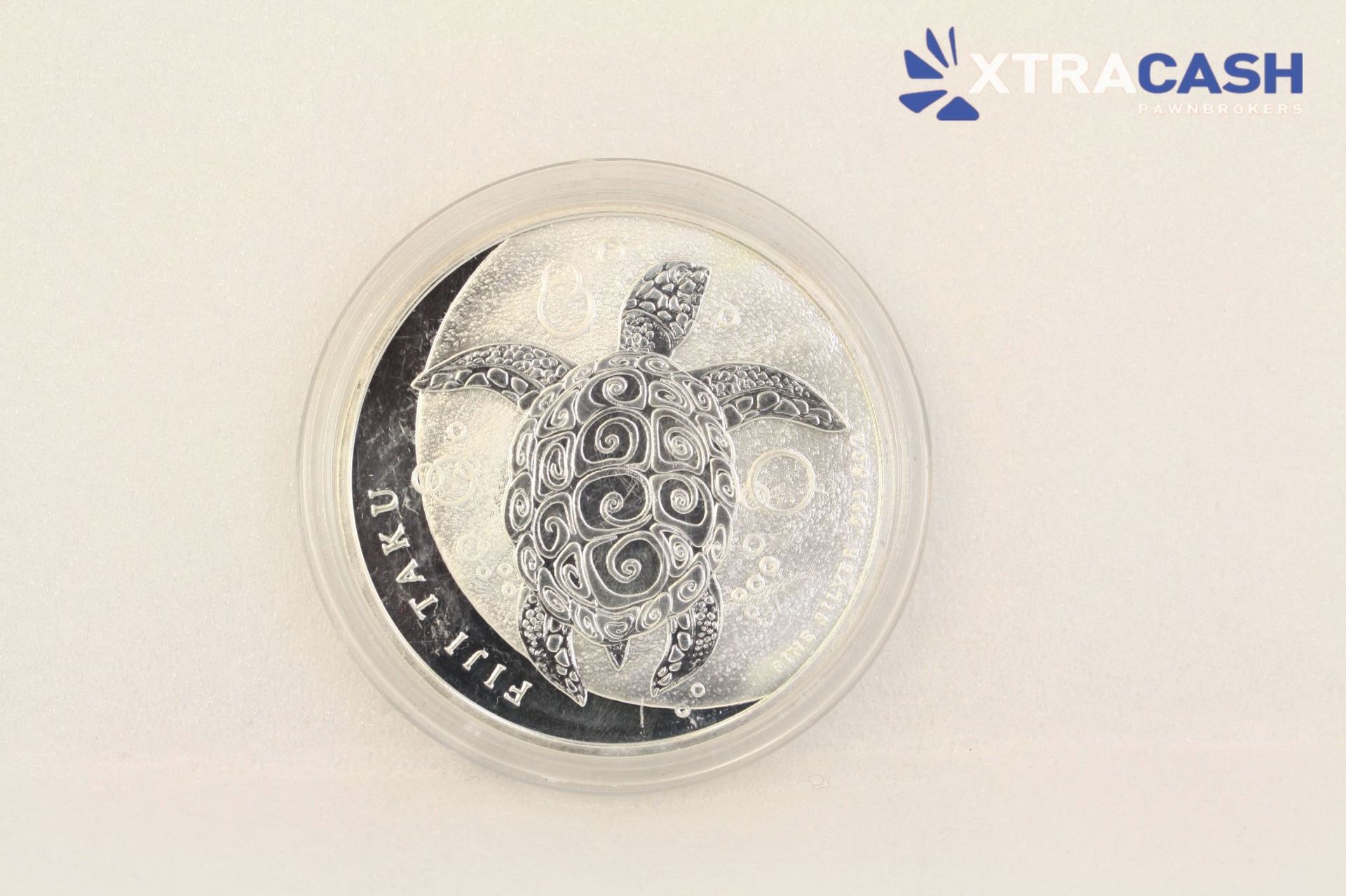 Round silver token or coin with a soccer player silhouette and XtraCash logo on a light background