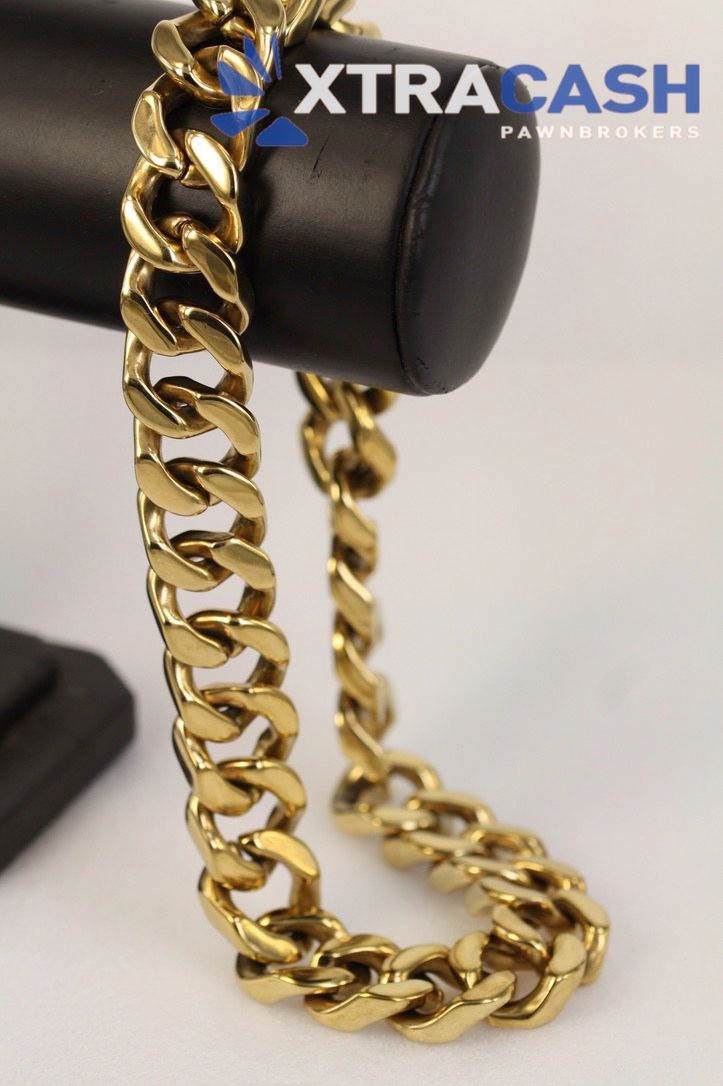 Gold Cuban link chain on a black display stand with XTRACASH logo.