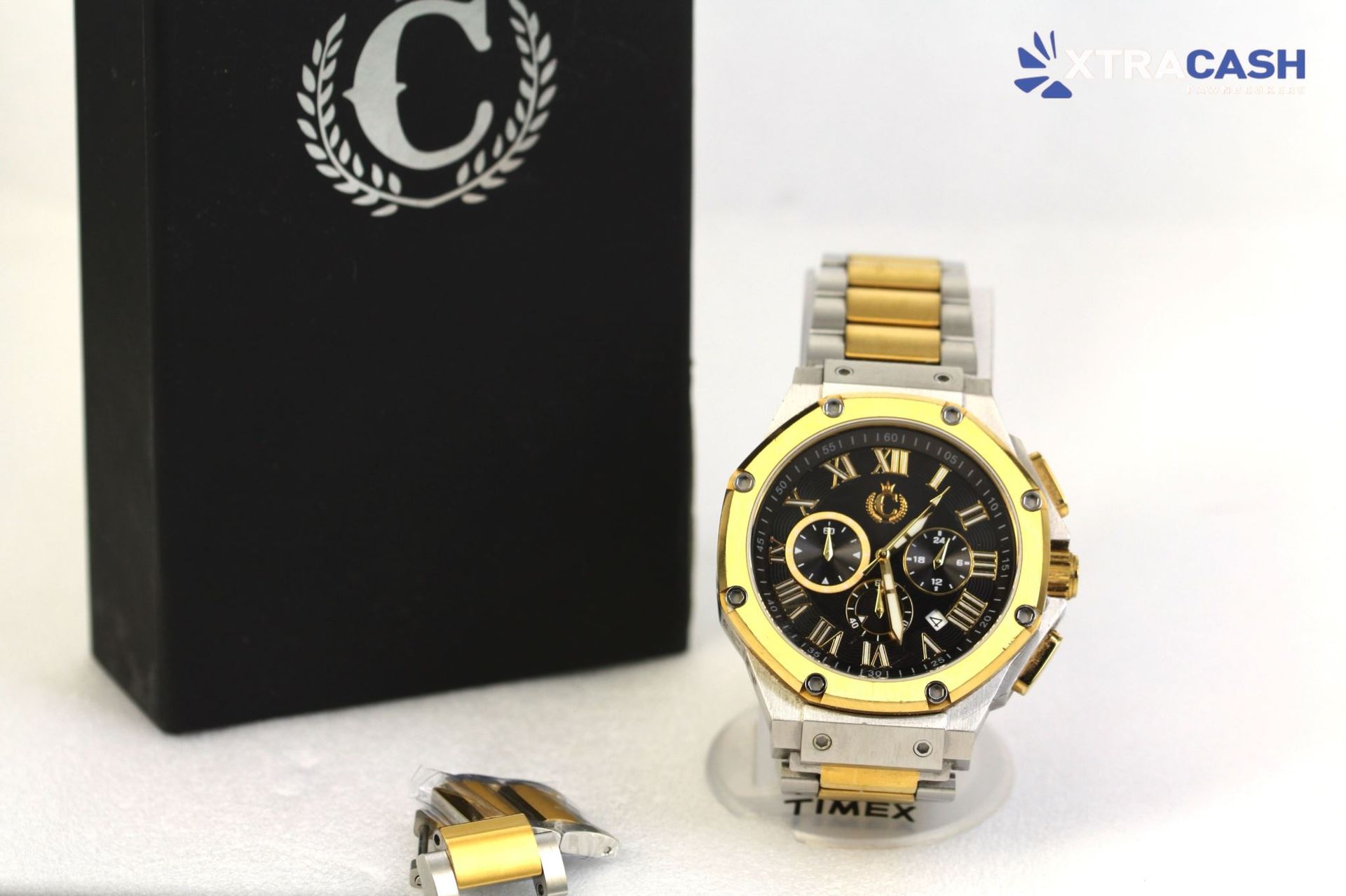 Gold-and-black wristwatch displayed beside a black box on a white surface