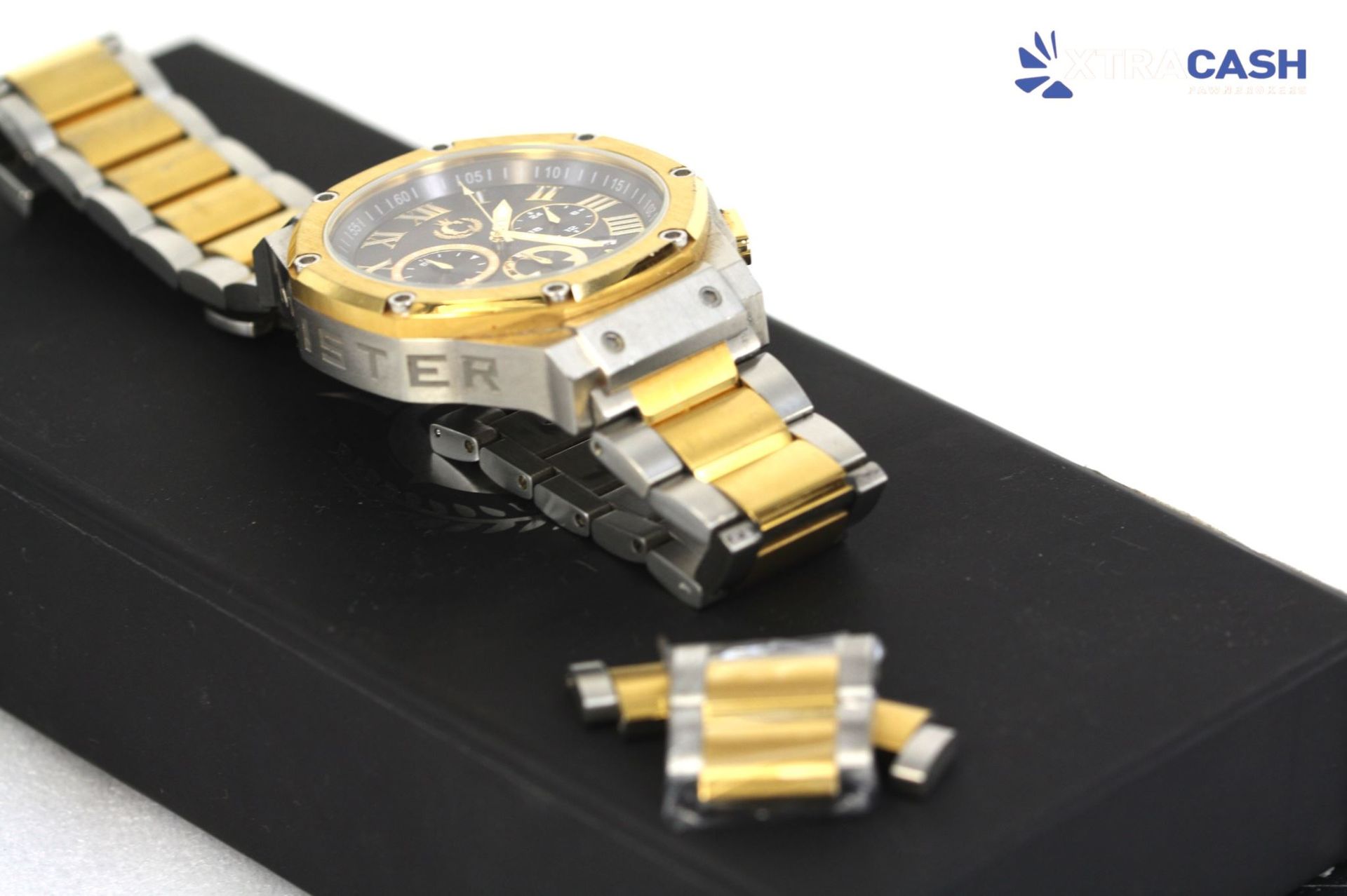 Gold-and-black wristwatch displayed beside a black box on a white surface
