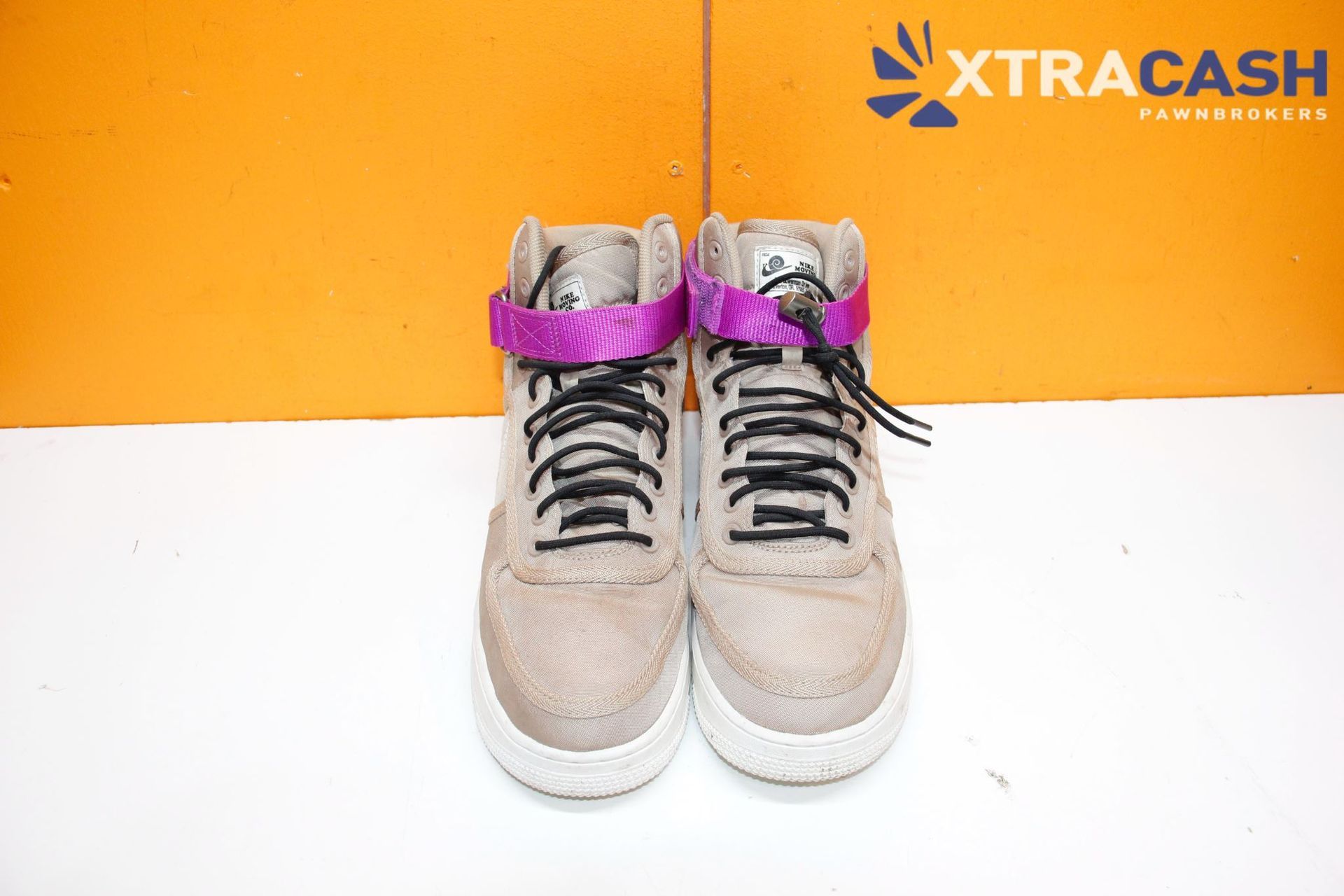 Two beige high-top sneakers with purple accents on a white surface against an orange background.
