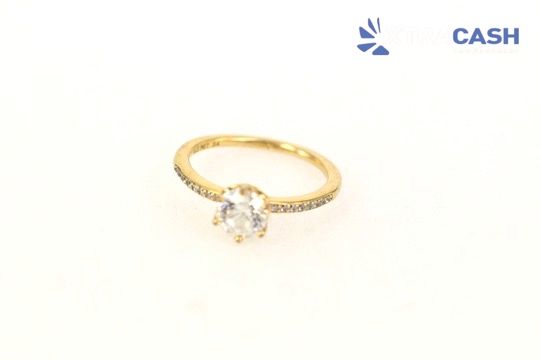 Gold ring with a clear gemstone on a white background, with a small “CASH” logo in the corner