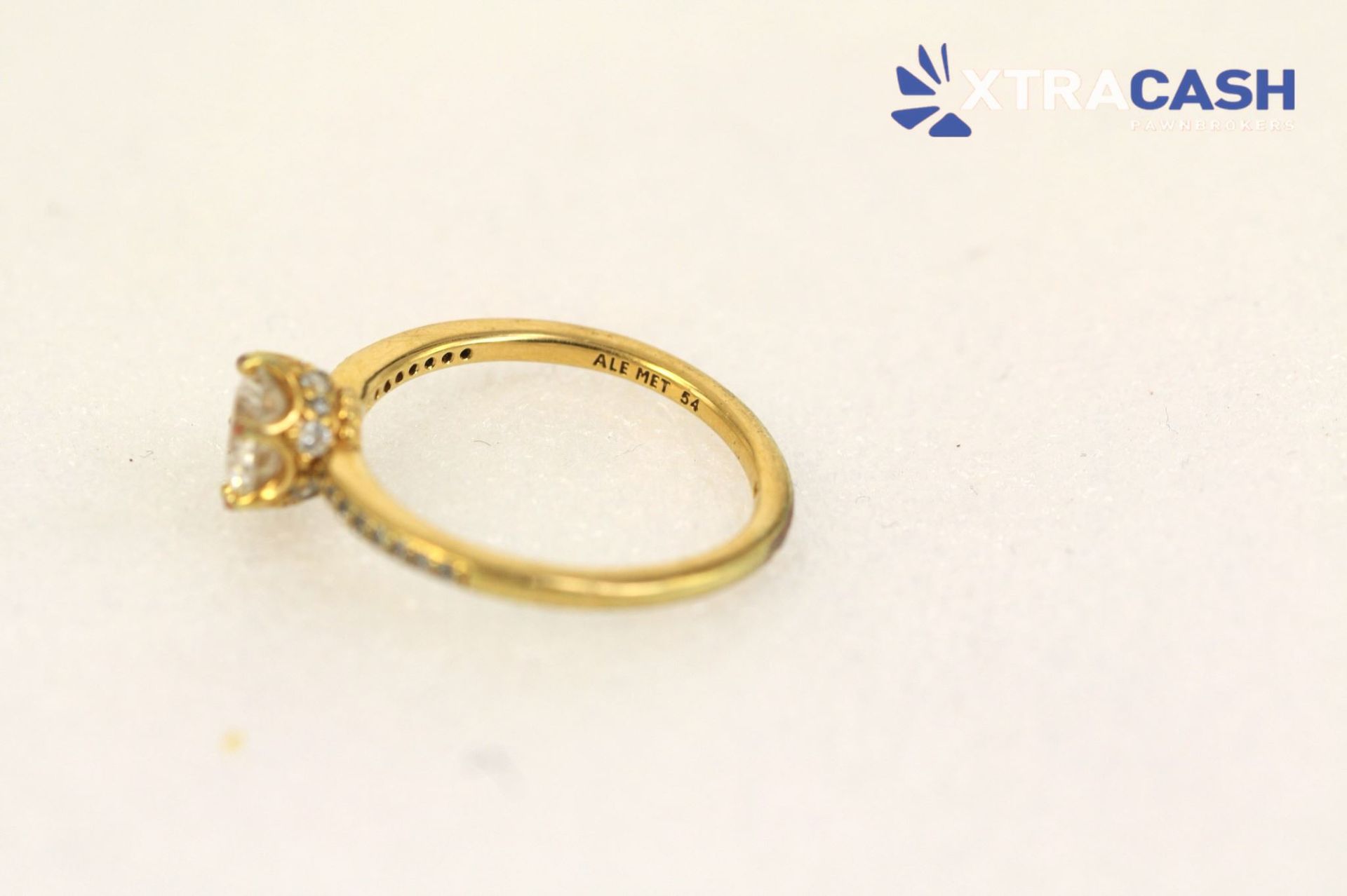 Gold ring with a clear gemstone on a white background, with a small “CASH” logo in the corner