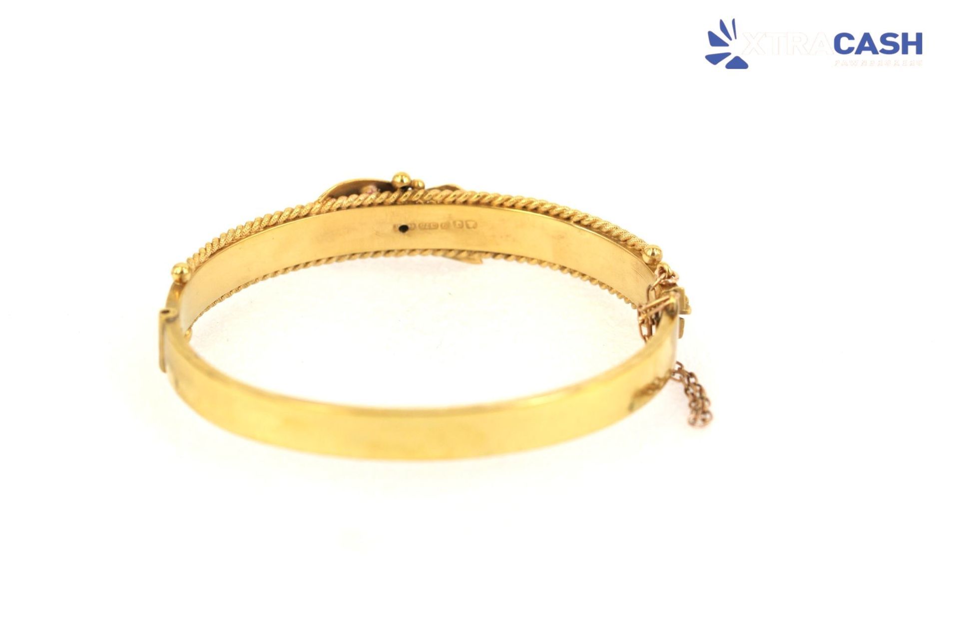 Gold bangle bracelet with engraved floral details on a white background