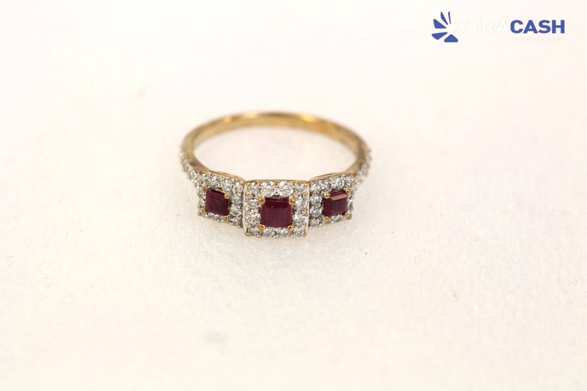 Gold ring with three red gemstones and small clear stones on a white background