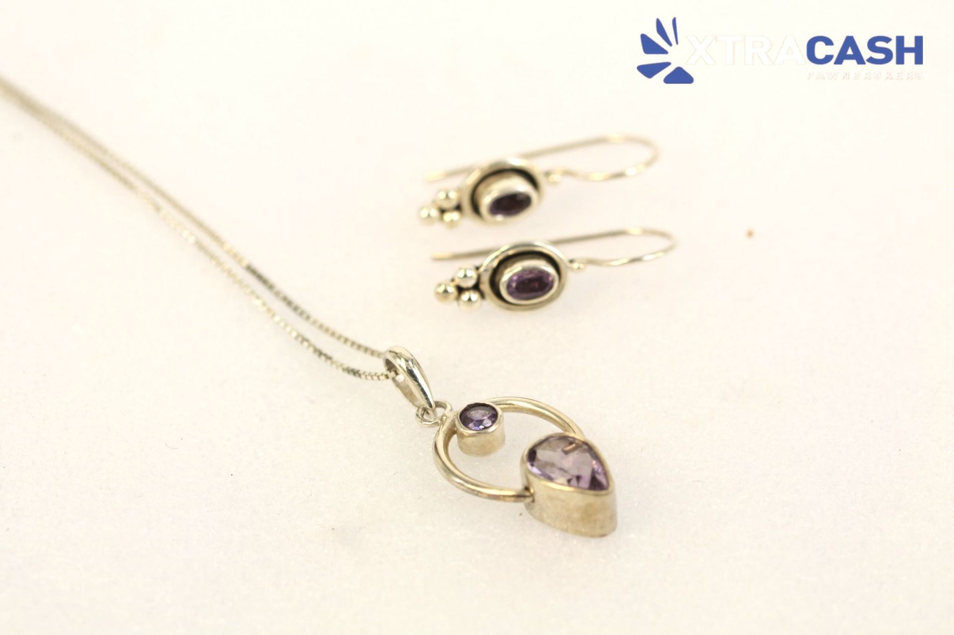 Gold necklace and matching earrings with purple stones on a white background
