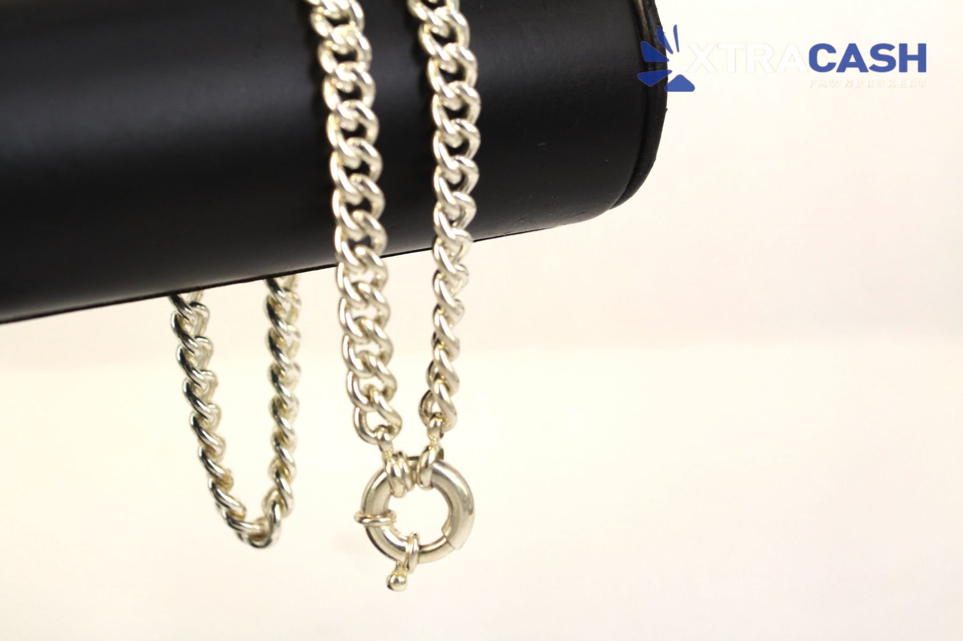 Silver chain bracelet draped over a black cylindrical rod on a light background