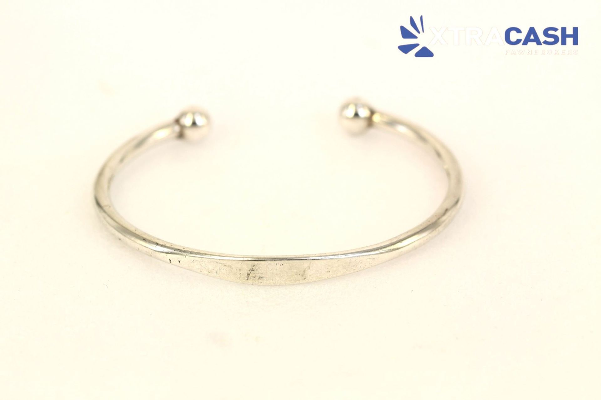 Silver open cuff bracelet with two round ends on a light background