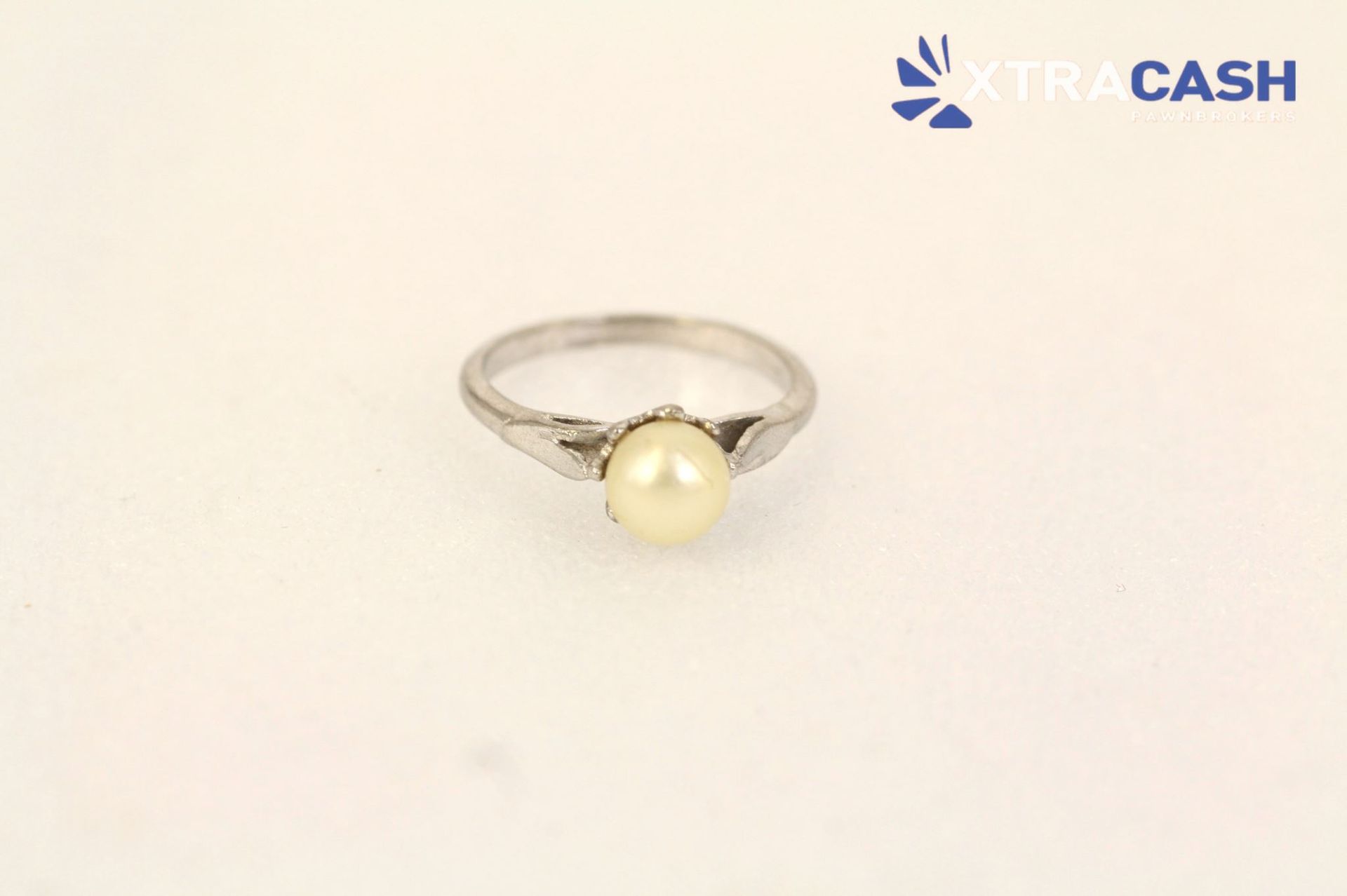 Silver ring with a round cream pearl on a light background
