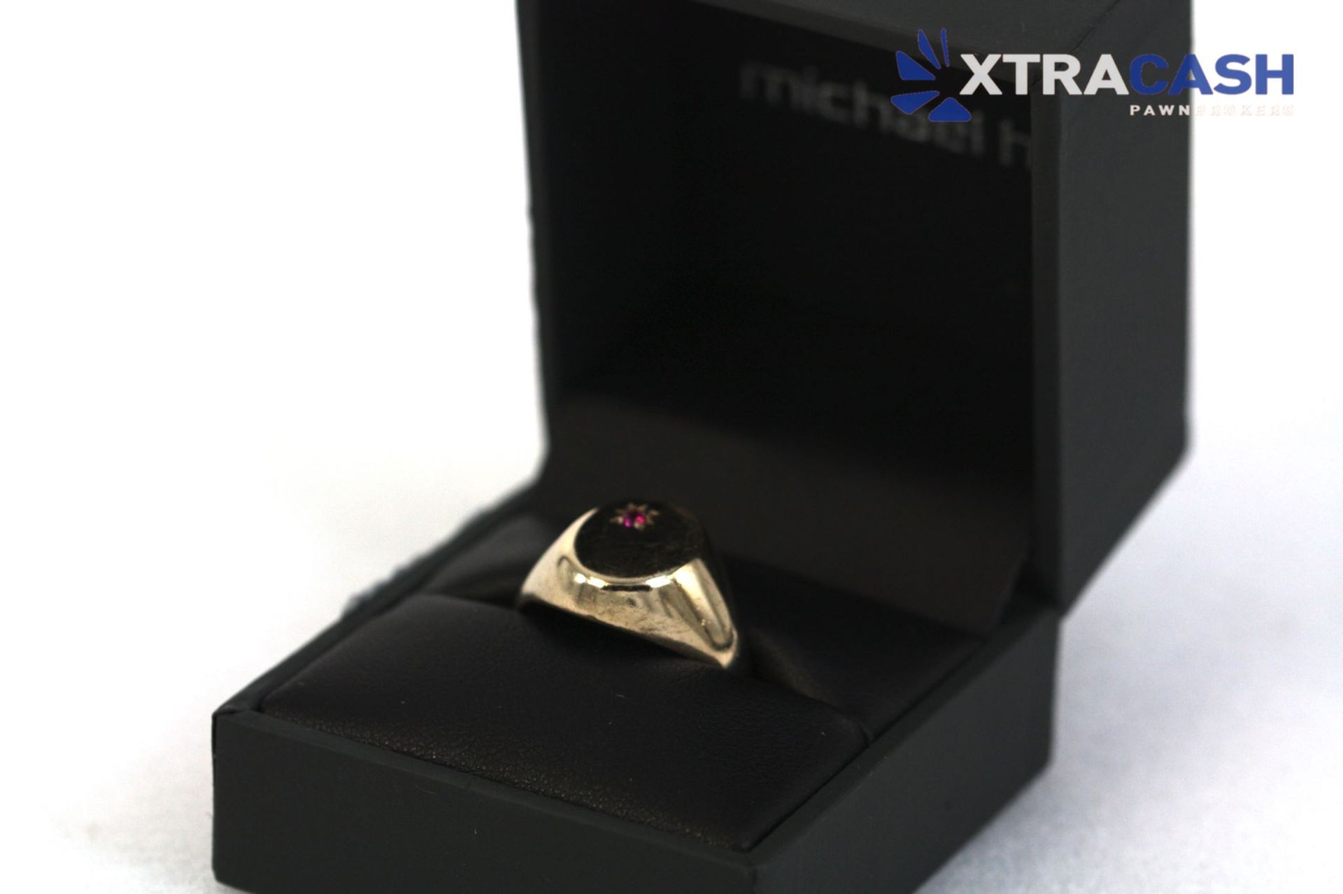 Black ring with a red stone displayed in an open black jewelry box on a white background