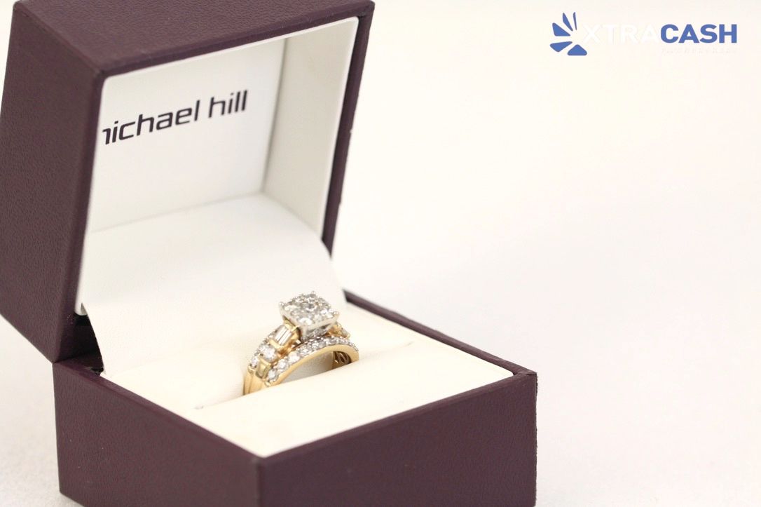 Open burgundy ring box with diamond ring and gold bands inside, Michael Hill logo visible