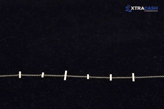 Delicate gold chain bracelet with bar accents on a dark background