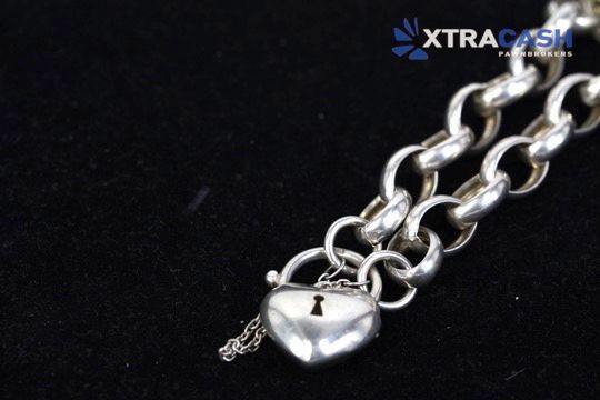 Silver chain necklace with a shiny heart-shaped pendant on a black background