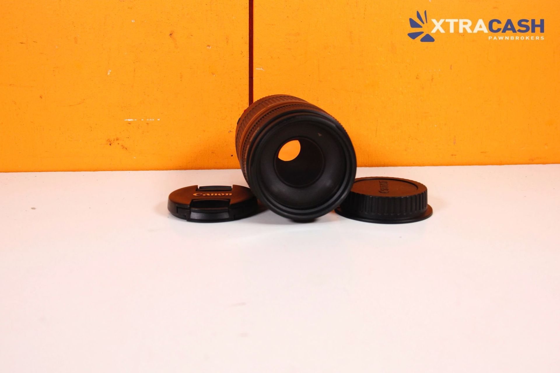 Camera lens with two black caps on a white surface against an orange background