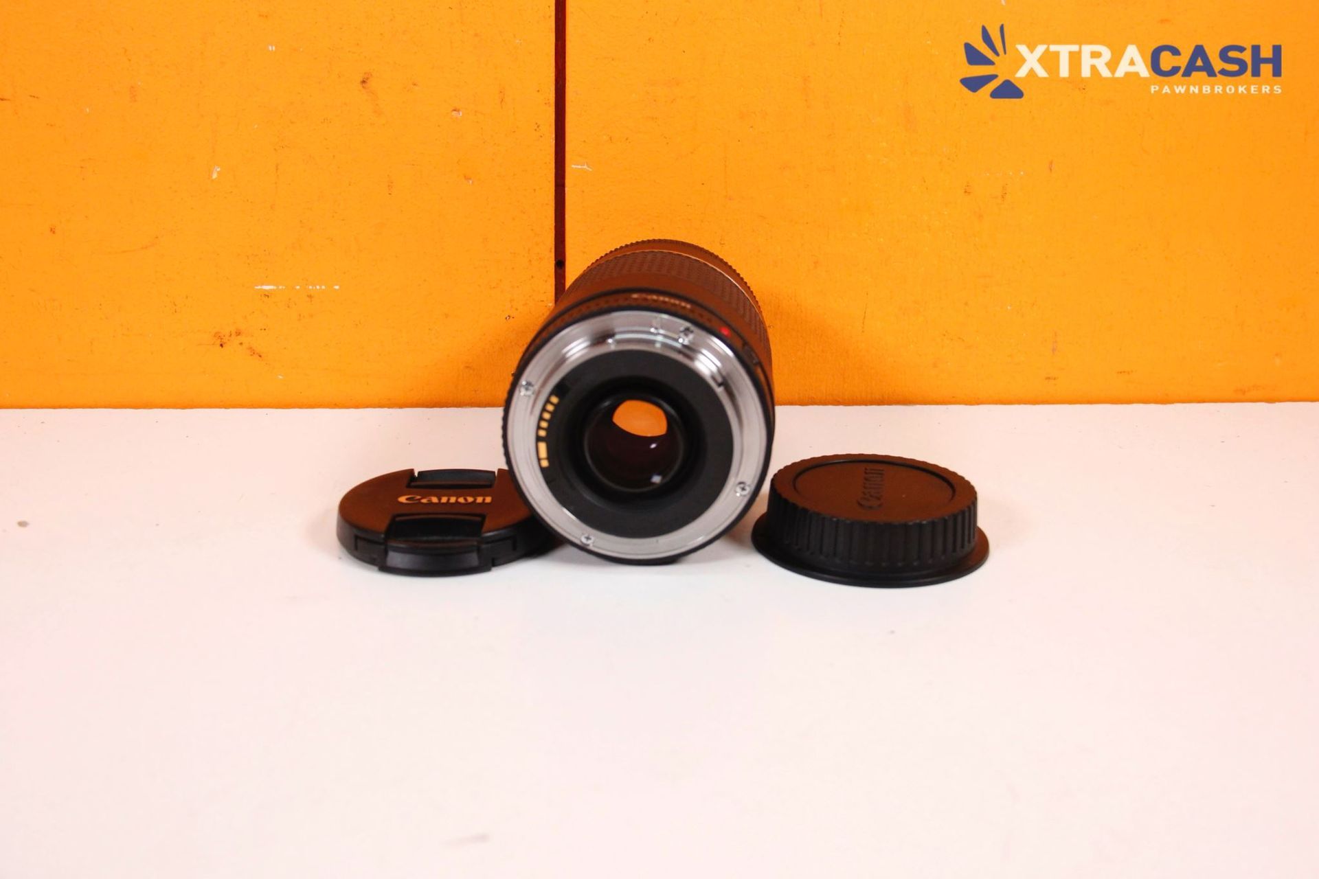 Camera lens with two black caps on a white surface against an orange background