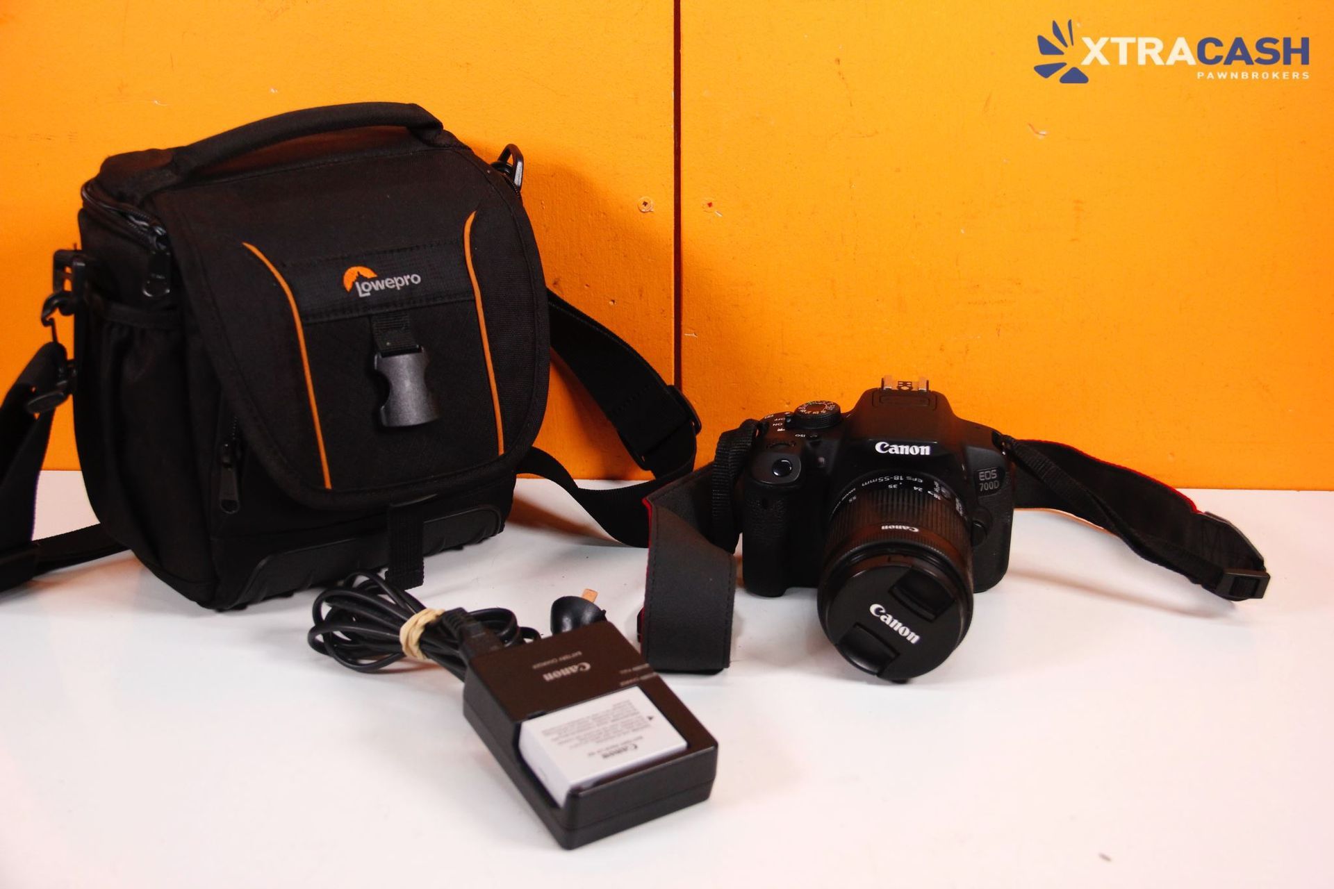 Black camera bag, DSLR camera, and battery charger on a white surface against an orange background.