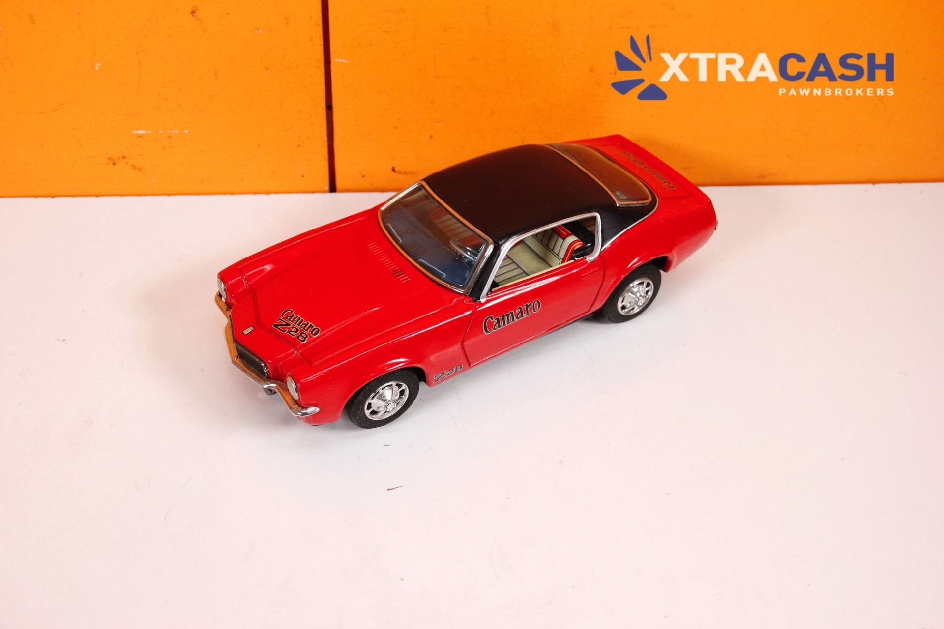 Red toy car on a white surface with an orange XTRACASH background