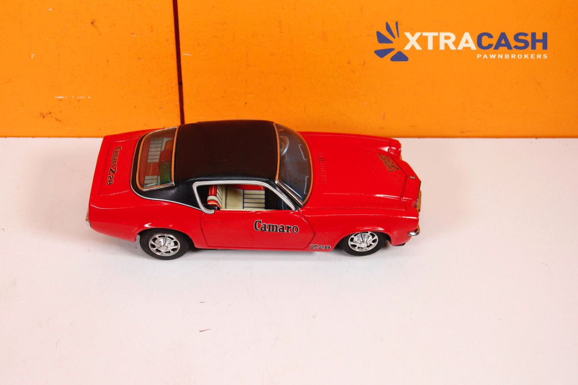 Red toy car on a white surface with an orange XTRACASH background