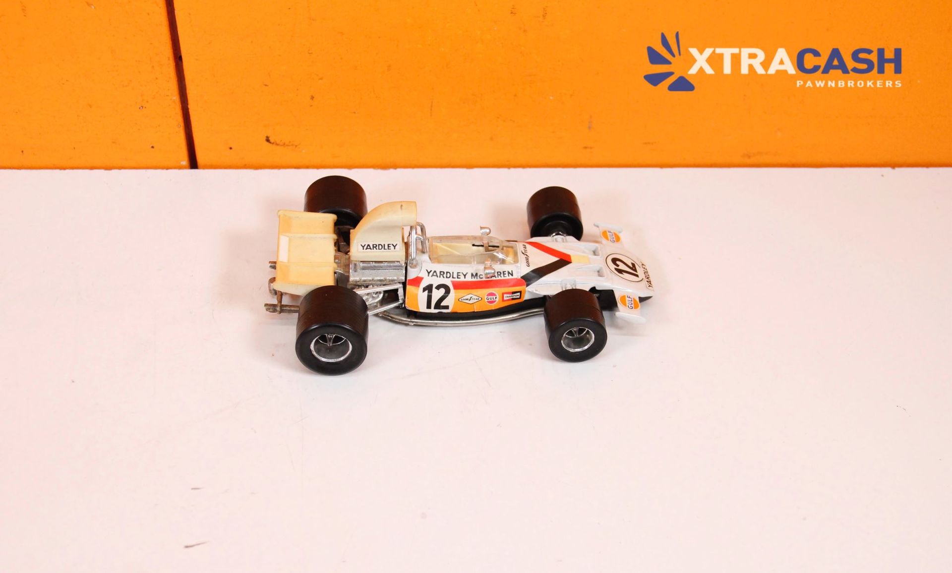 White-and-orange toy race car with number 12 on a plain white surface against an orange background.