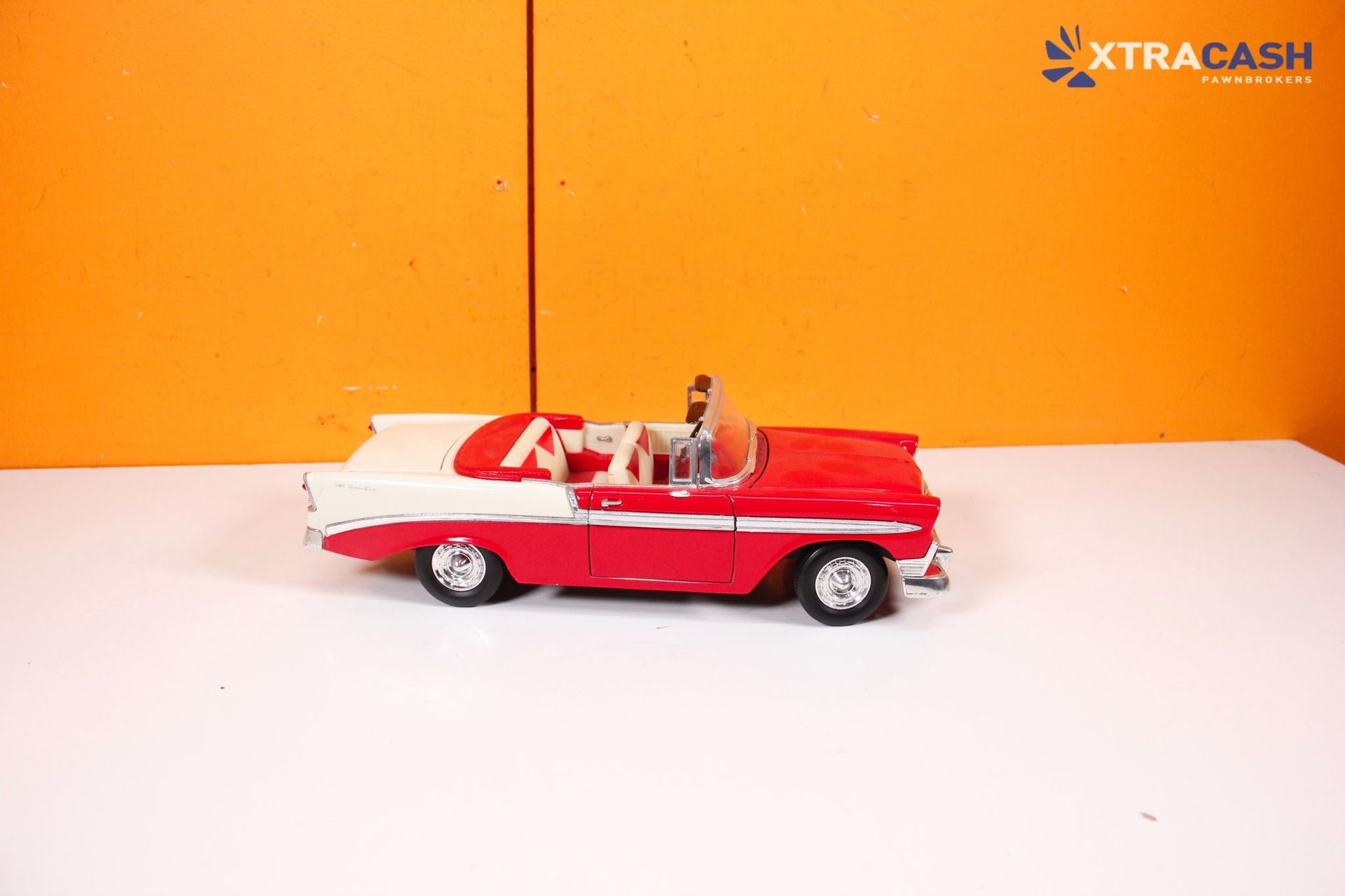Red toy convertible car on a white surface against an orange background.