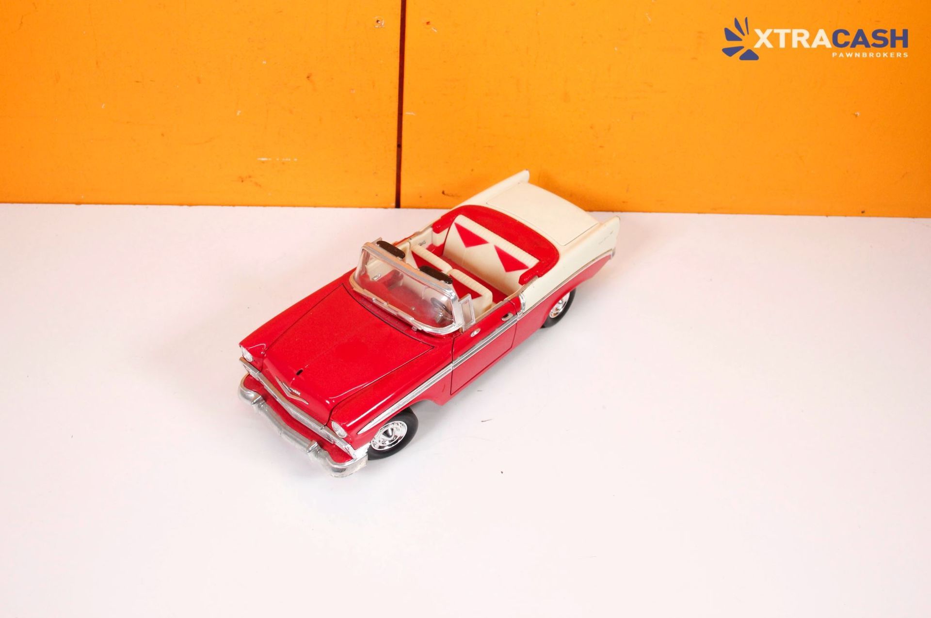 Red toy convertible car on a white surface against an orange background.