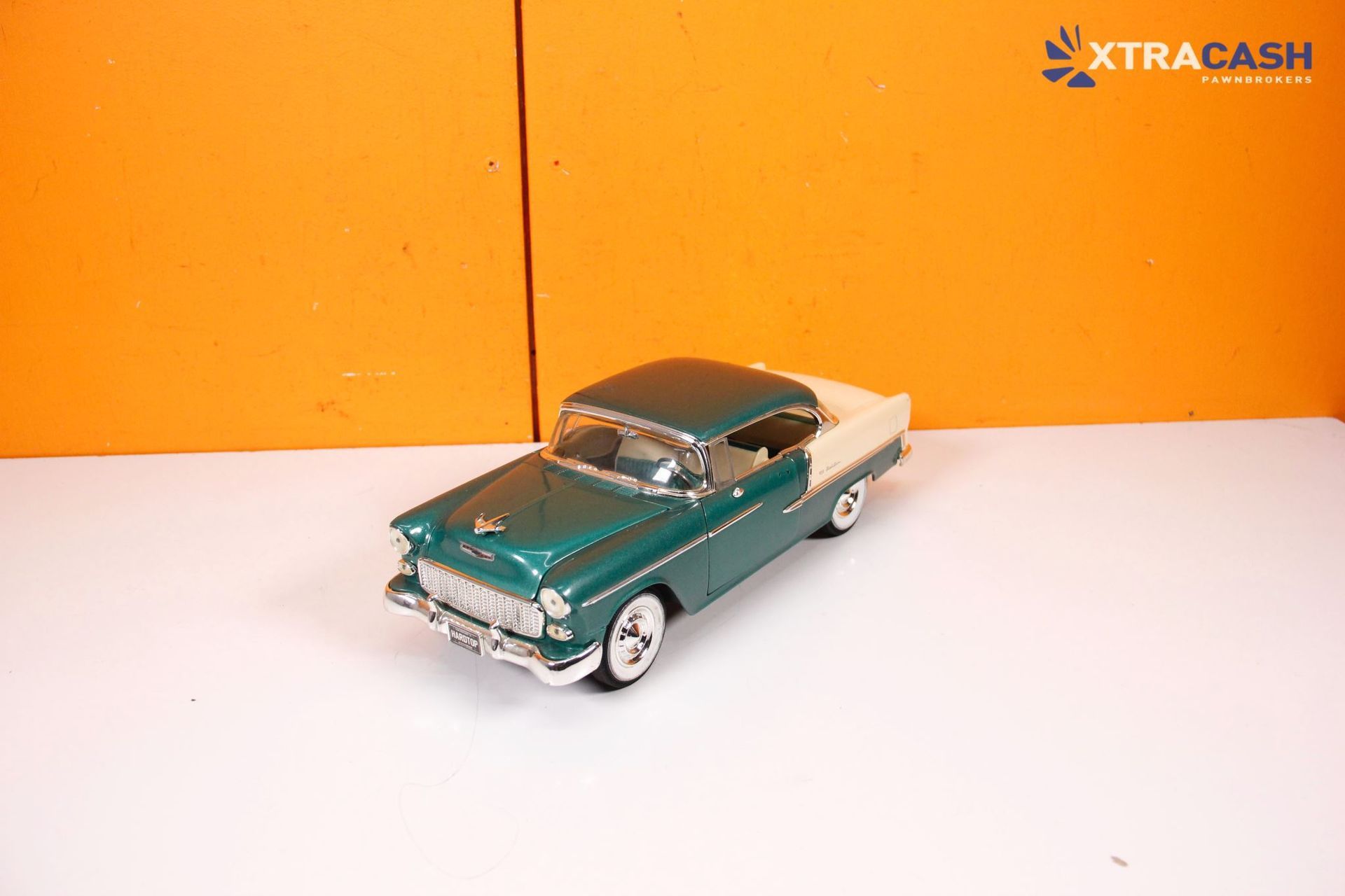 Teal toy convertible car on a white surface against an orange background
