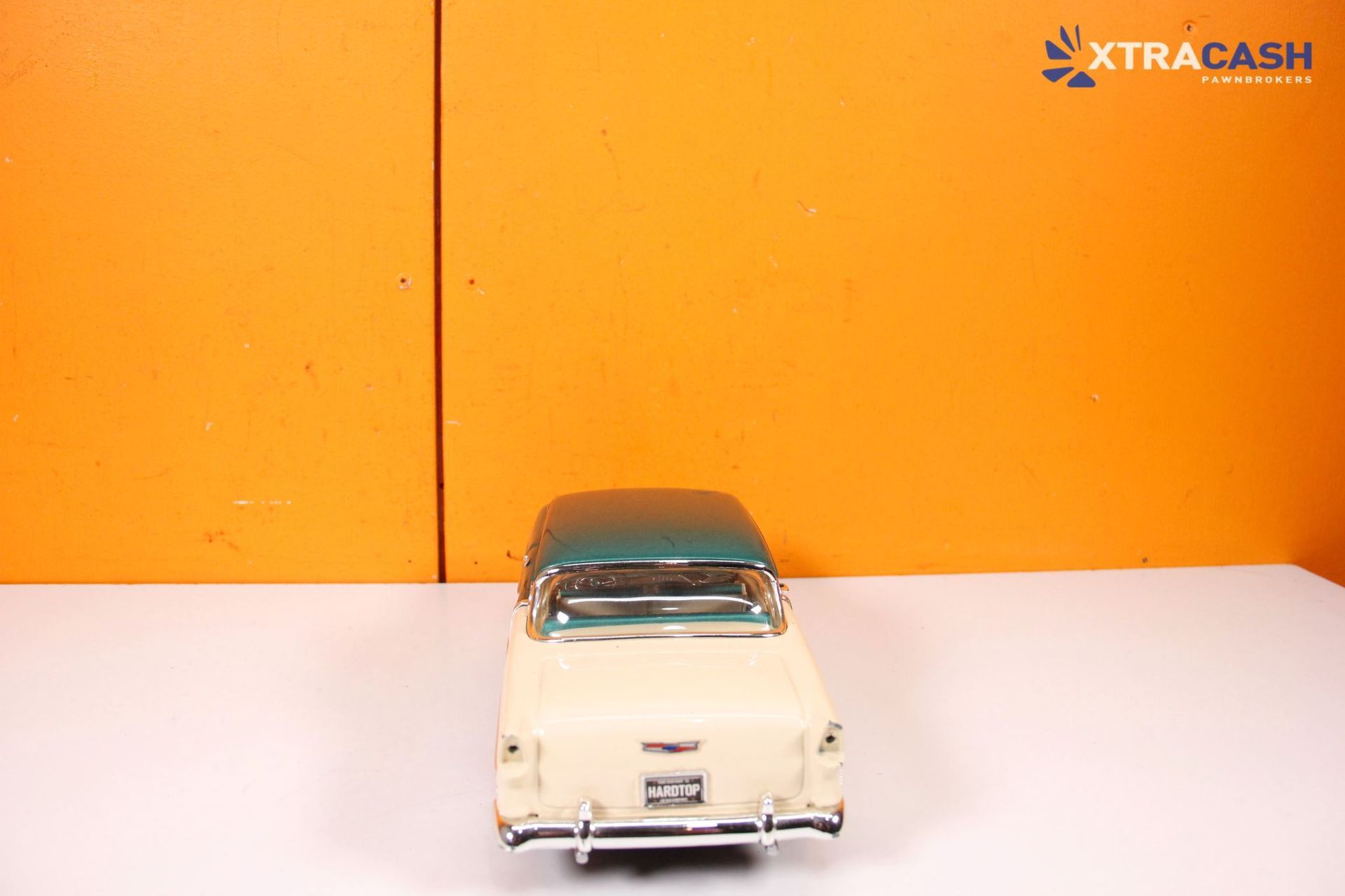 Teal toy convertible car on a white surface against an orange background