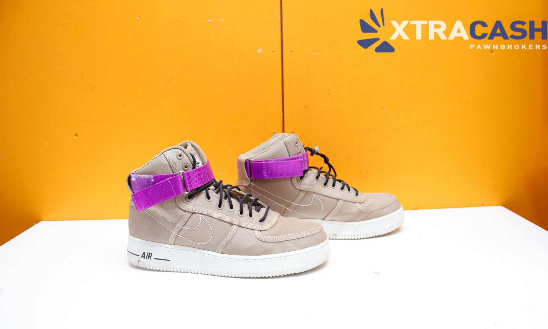 Two beige high-top sneakers with purple accents on a white surface against an orange background.