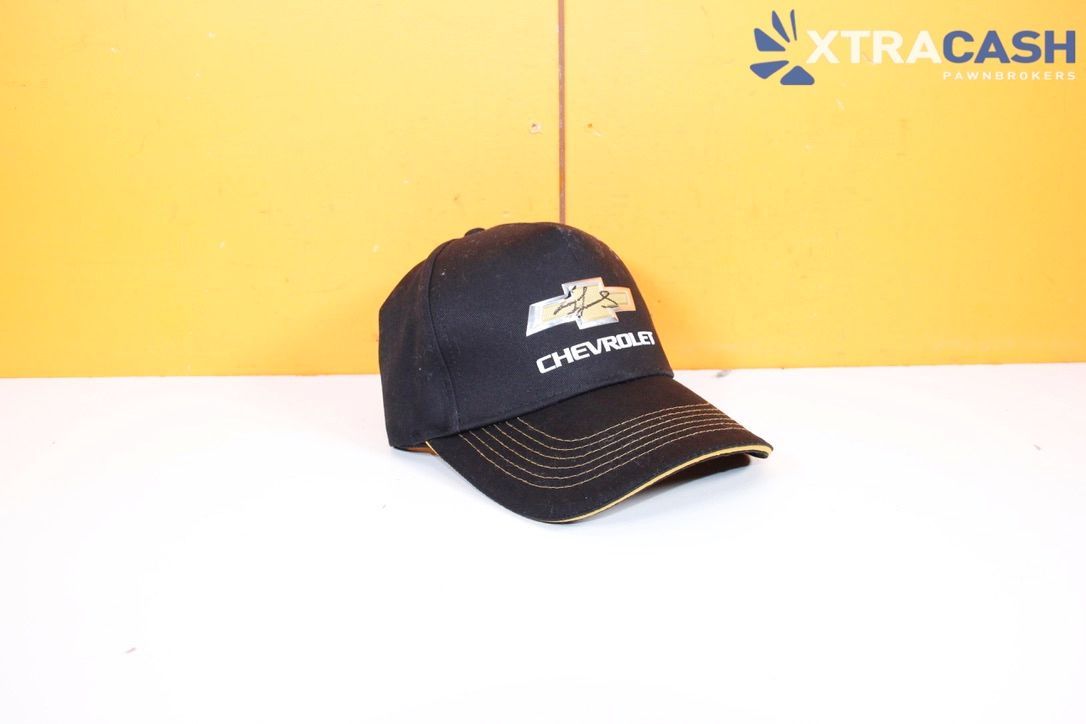 Black Chevrolet cap with white logo, on a white surface against a yellow background.