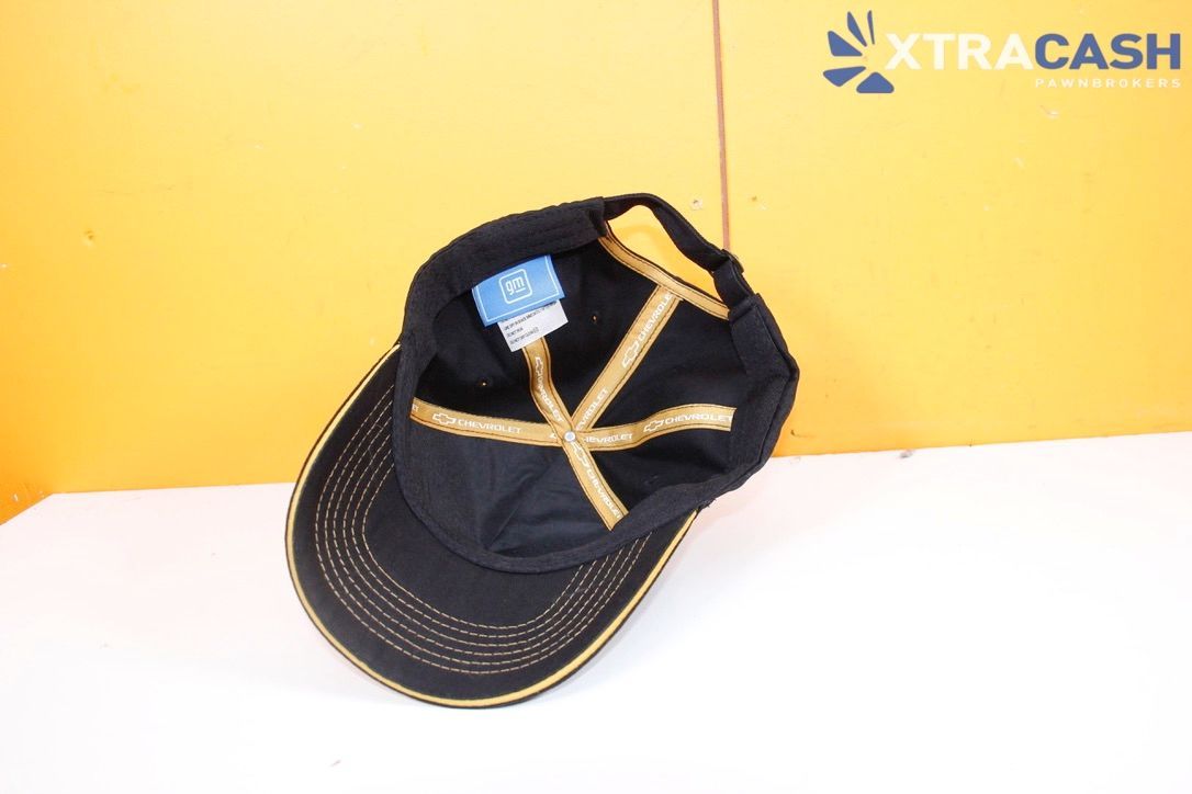 Black Chevrolet cap with white logo, on a white surface against a yellow background.