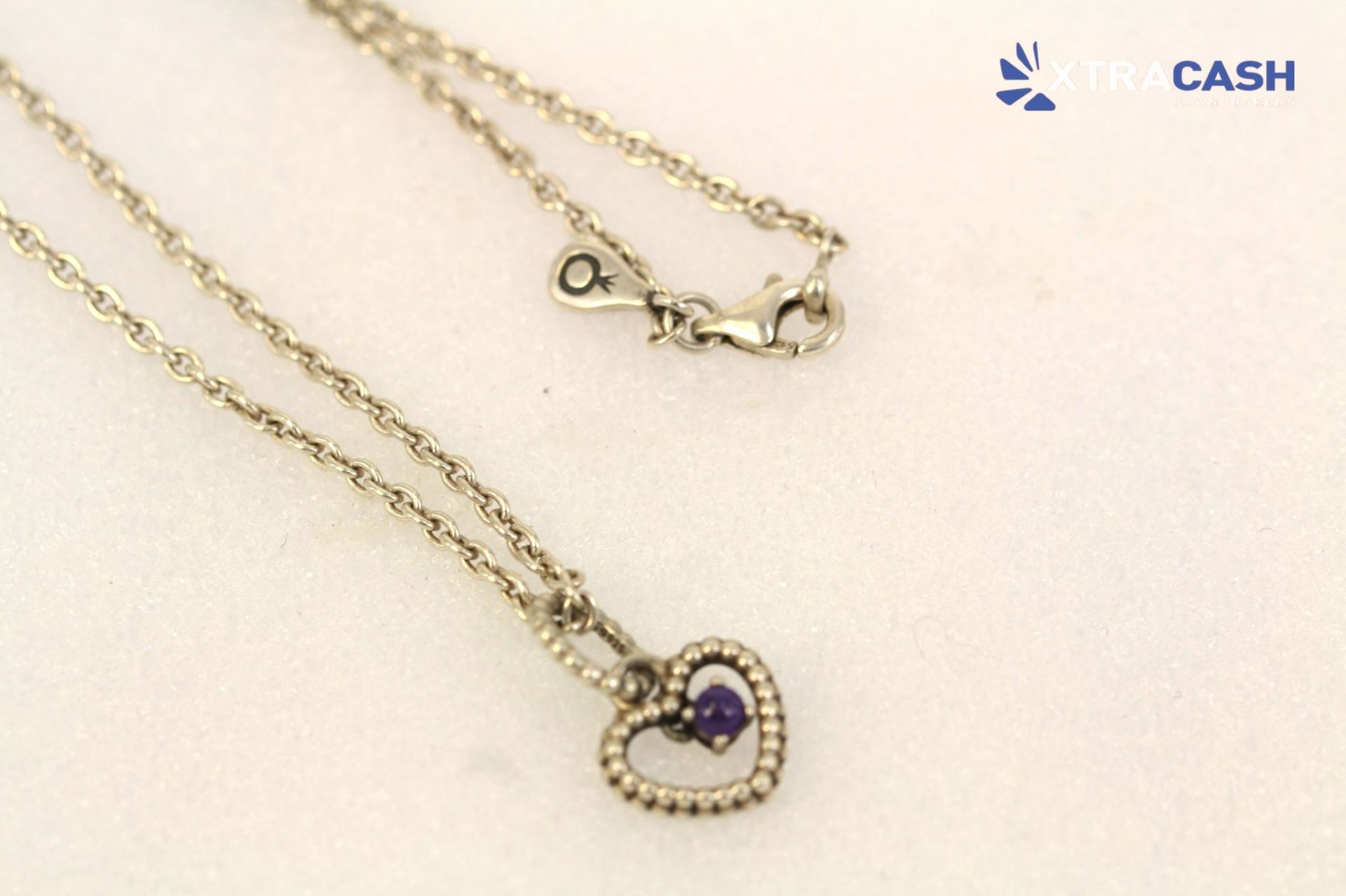 Two gold necklaces with a heart pendant and a purple gemstone on a light background