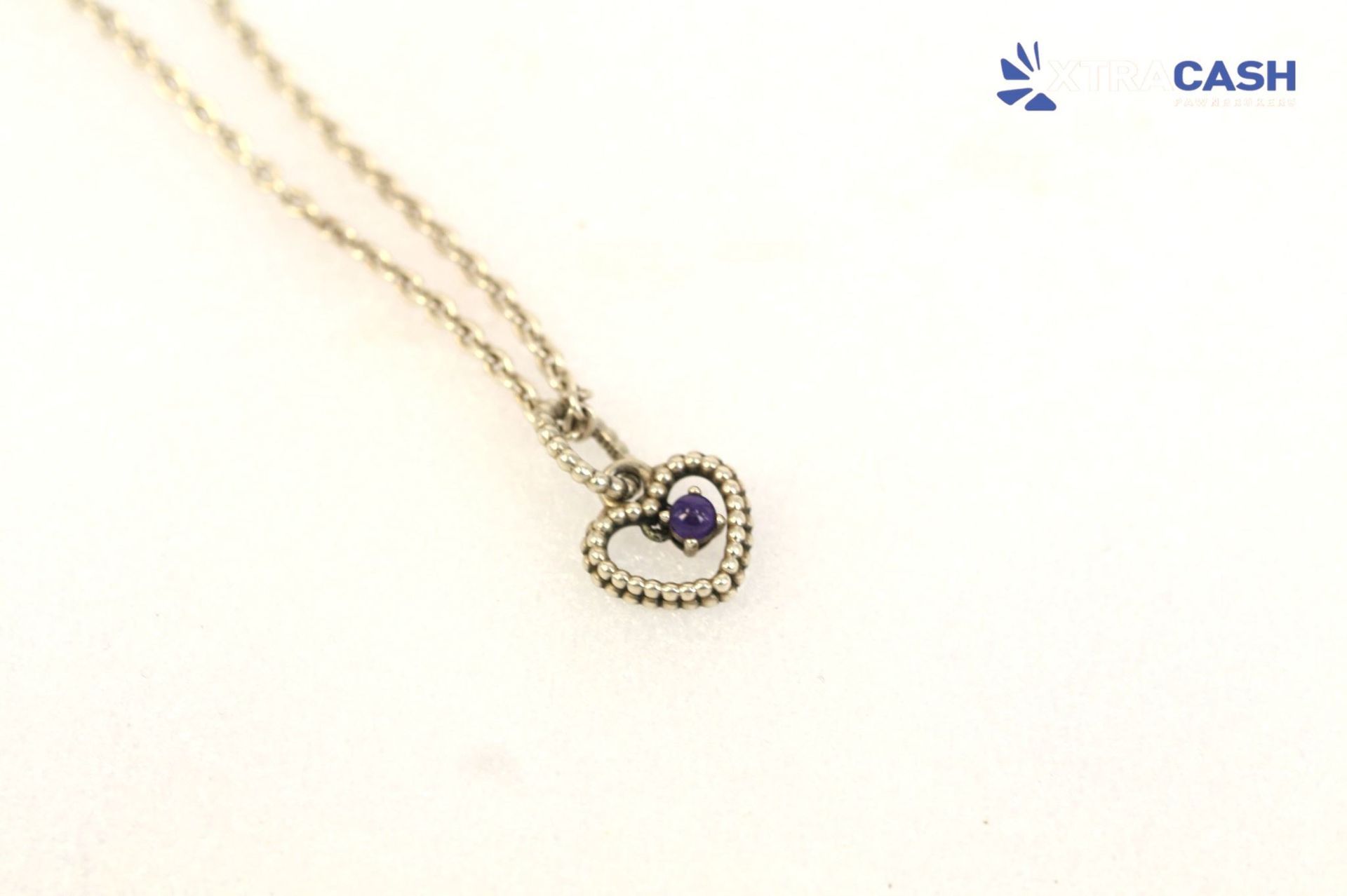 Two gold necklaces with a heart pendant and a purple gemstone on a light background