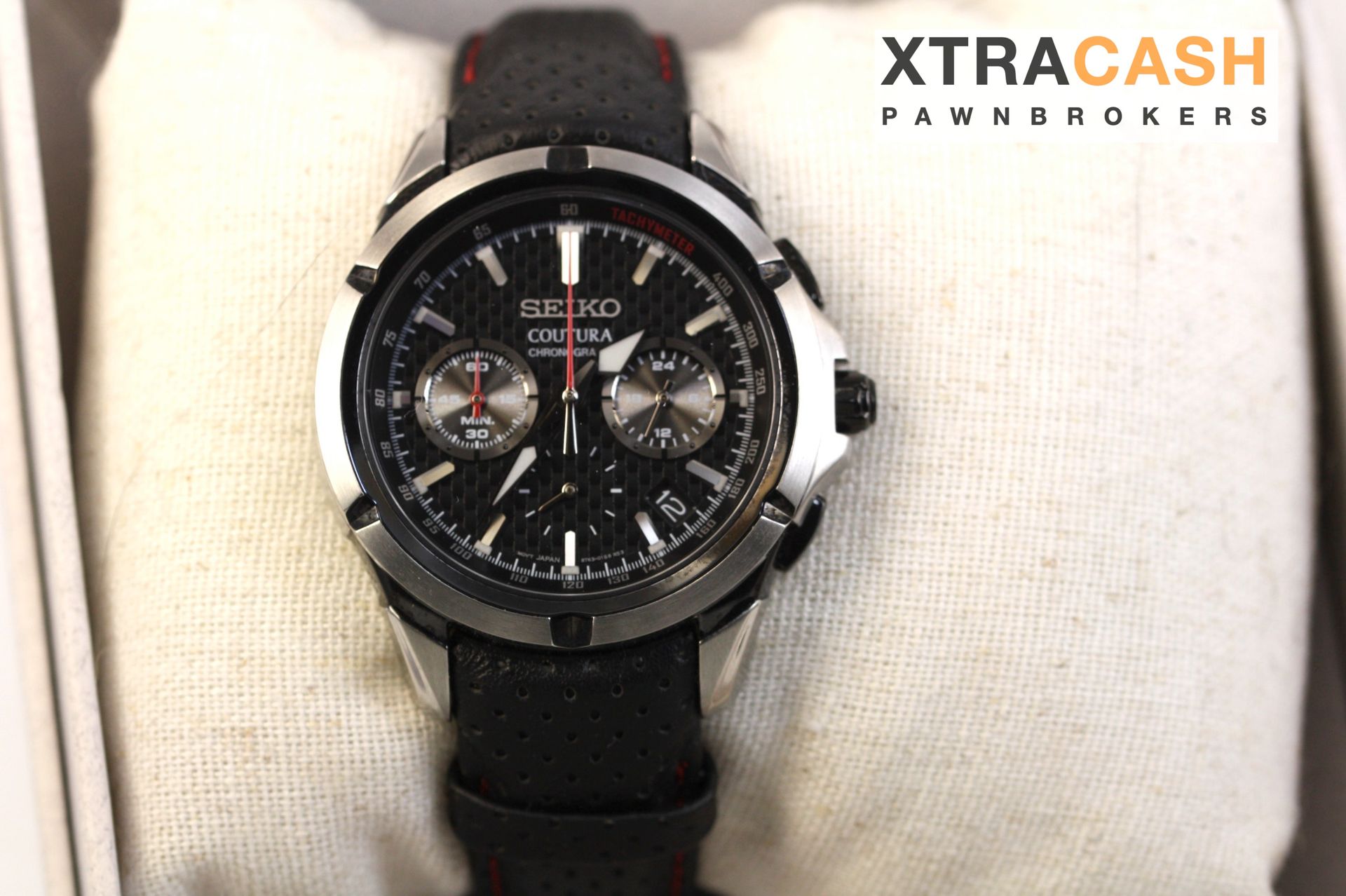 Black wristwatch on a white cushion beside an XtraCash Pawn Brokers card