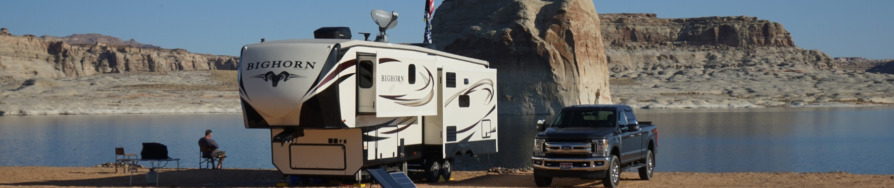 a rv is being towed by a truck by a lake .