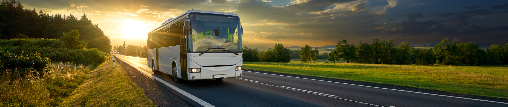 a bus is driving down a country road at sunset .