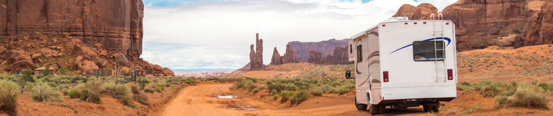 a white rv is driving down a dirt road in the desert .