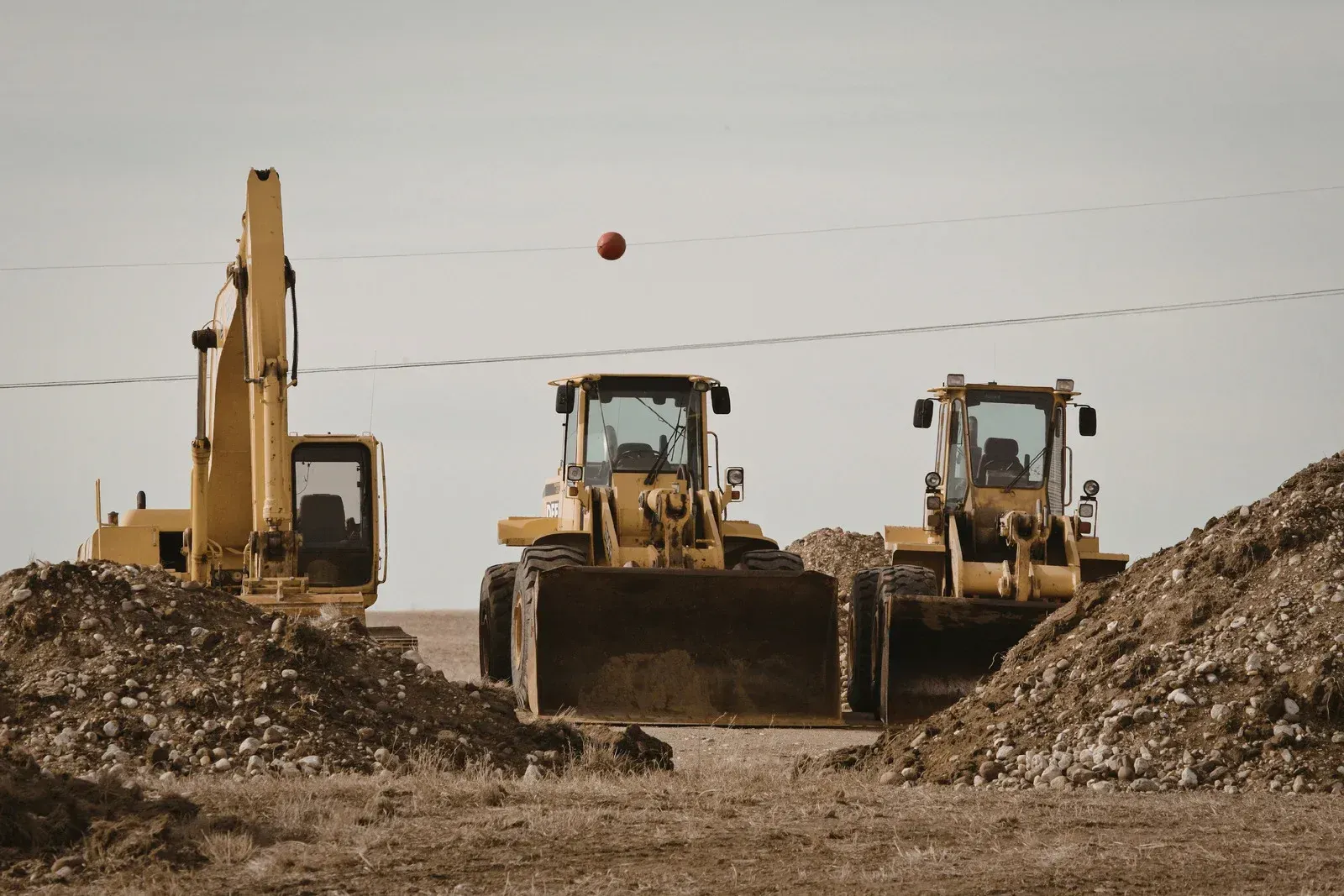 Yellow construction vehicles on a dirt site, with a loader centered between mounds of gravel.