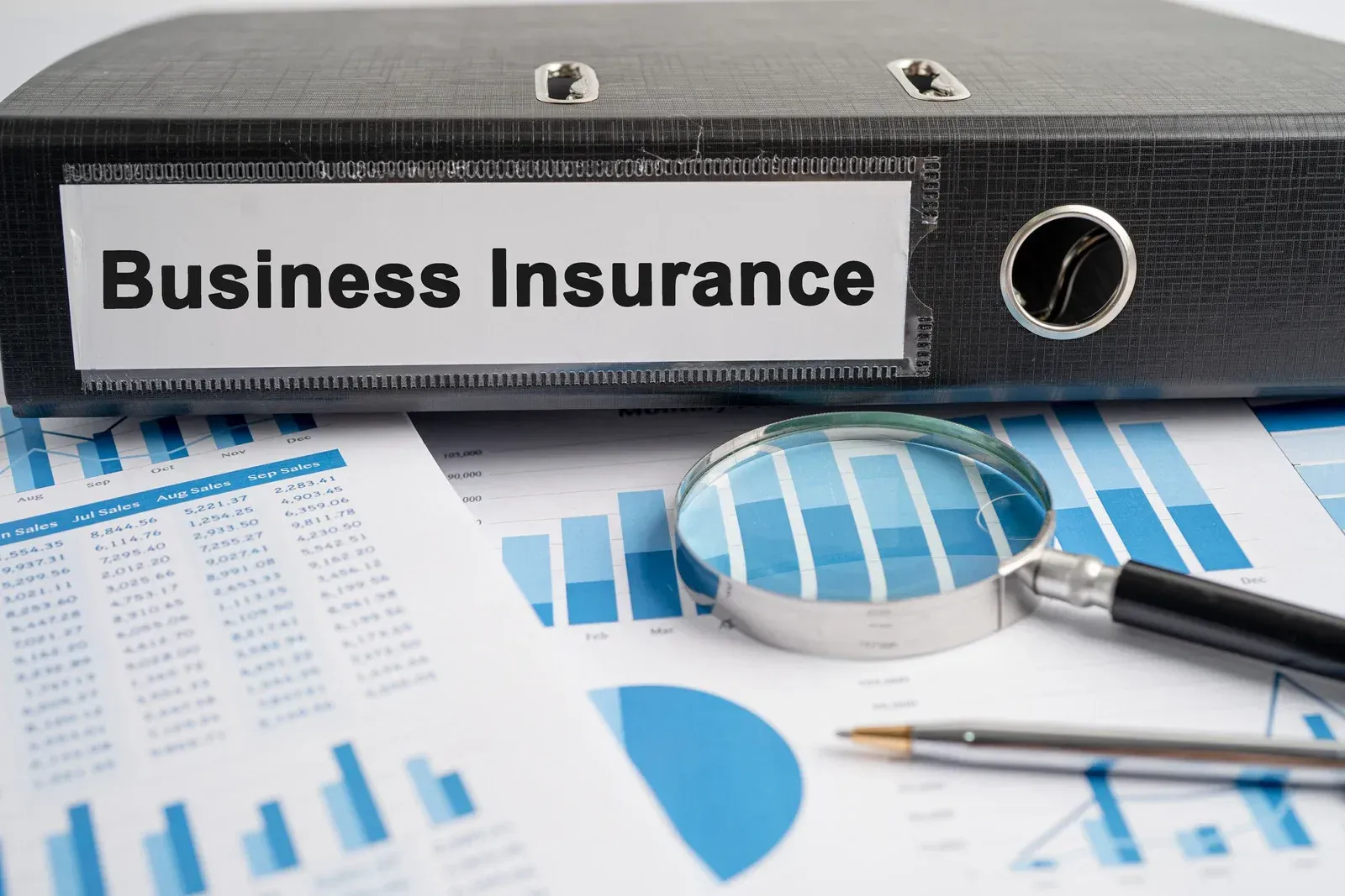 Business insurance binder on financial charts with magnifying glass and pen