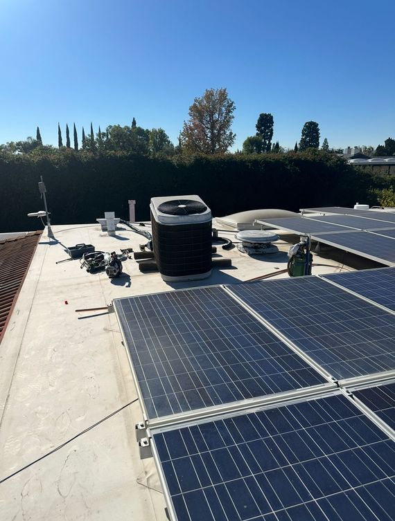 Solar panels on a rooftop under a clear blue sky, with HVAC units and trees in the background